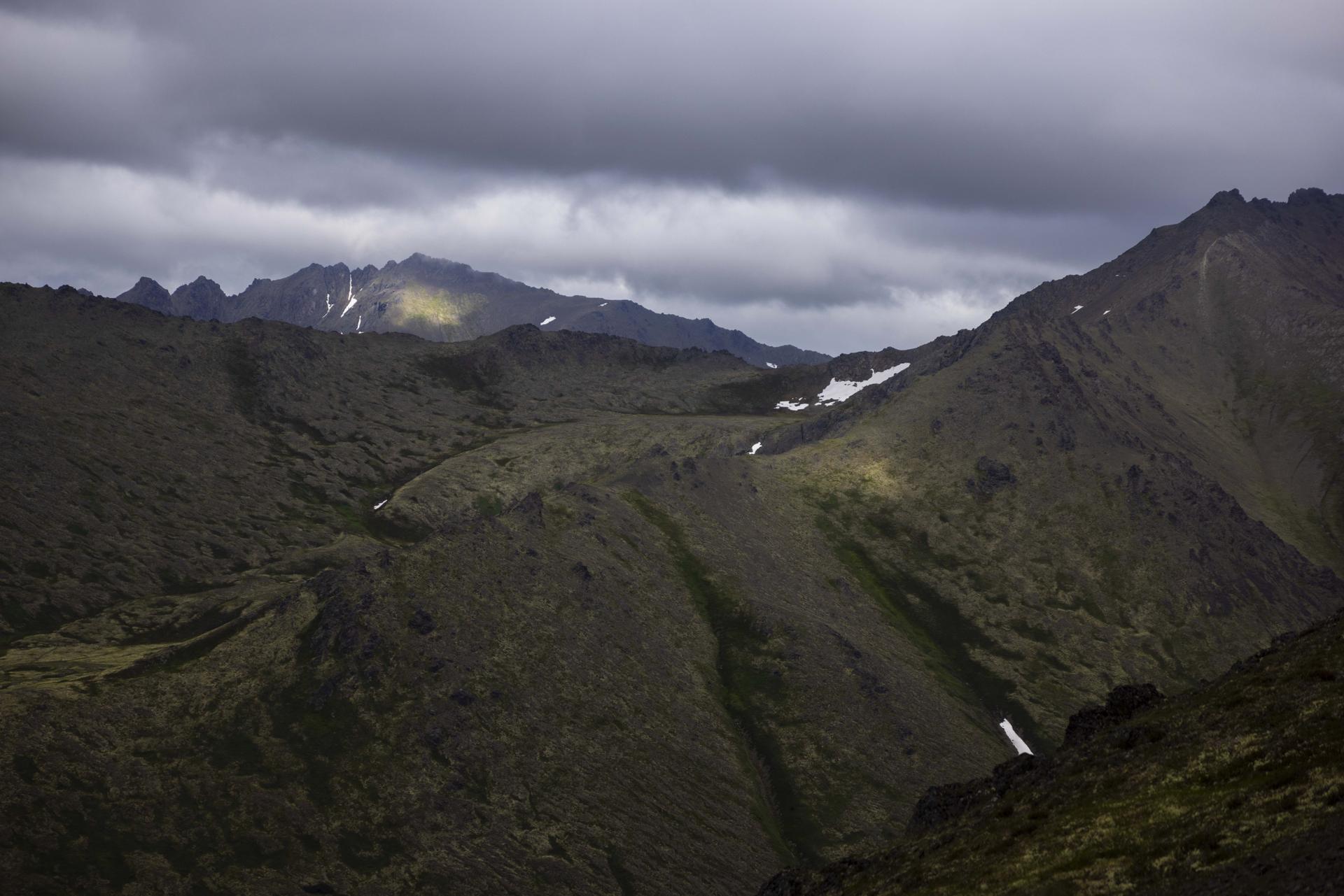 Dark, rugged mountains with patches of snow under a dramatic cloudy sky.