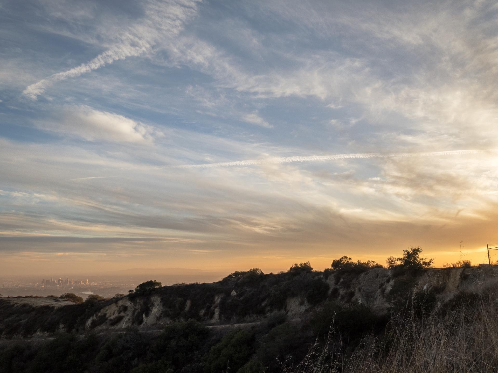 Sunset over a hilly landscape with wispy clouds and warm light.