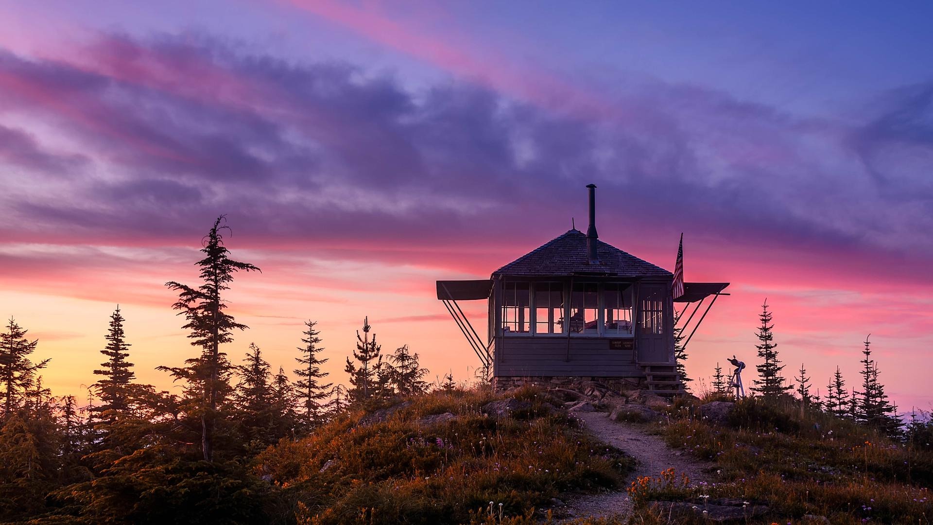 Fire lookout tower on a mountain top under a vibrant pink and purple sky.