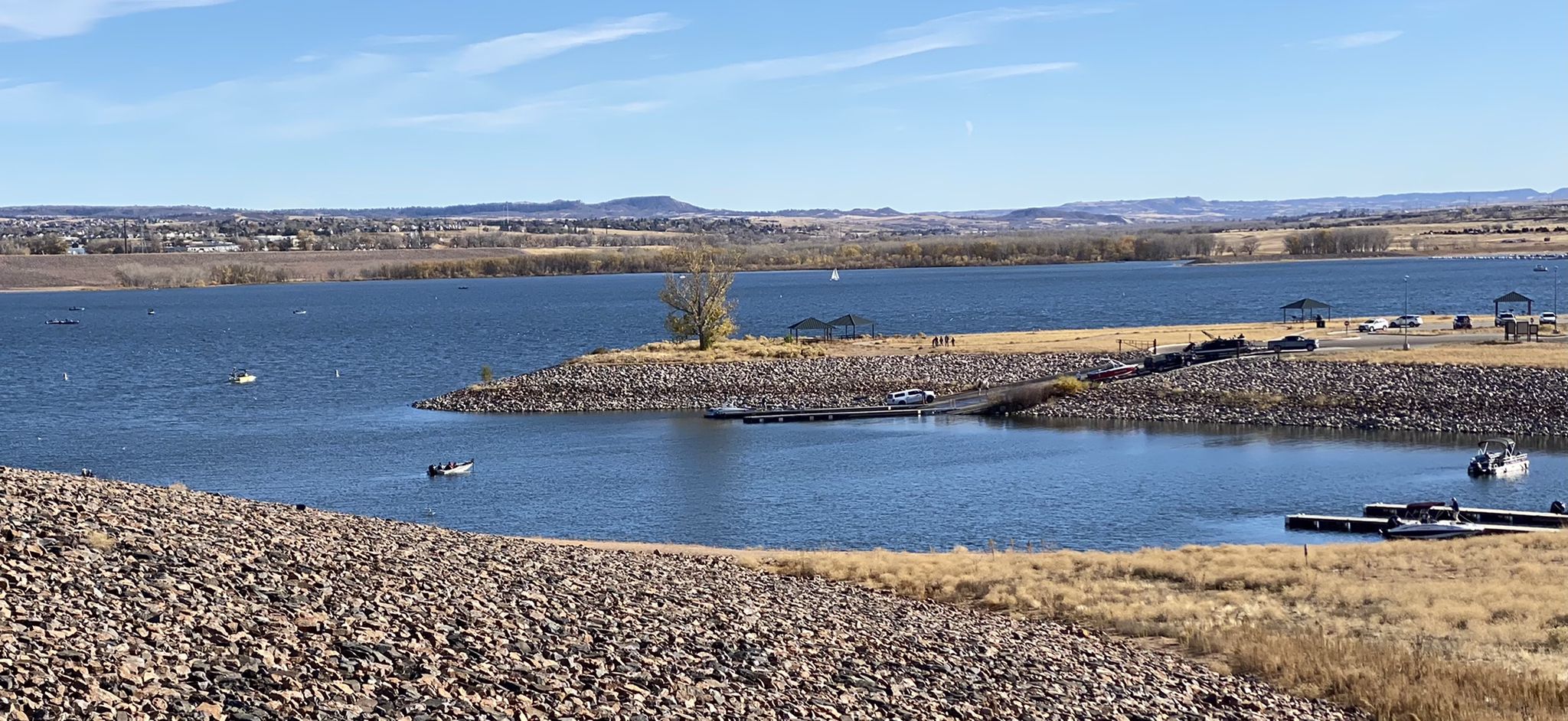 Wide view of a lake with rocky shores, boats, and distant land under a clear sky. - C-470 and Mary Carter Greenway Loop