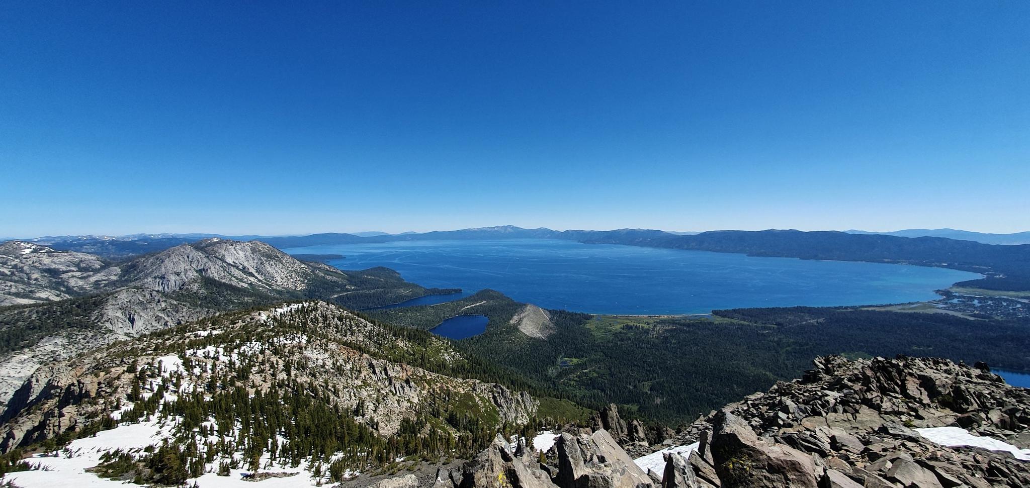 Panoramic view of a vast blue lake surrounded by snowy and rocky mountains.