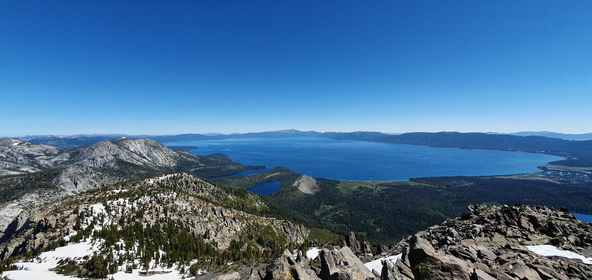 Panoramic view of a vast blue lake surrounded by snowy and rocky mountains.