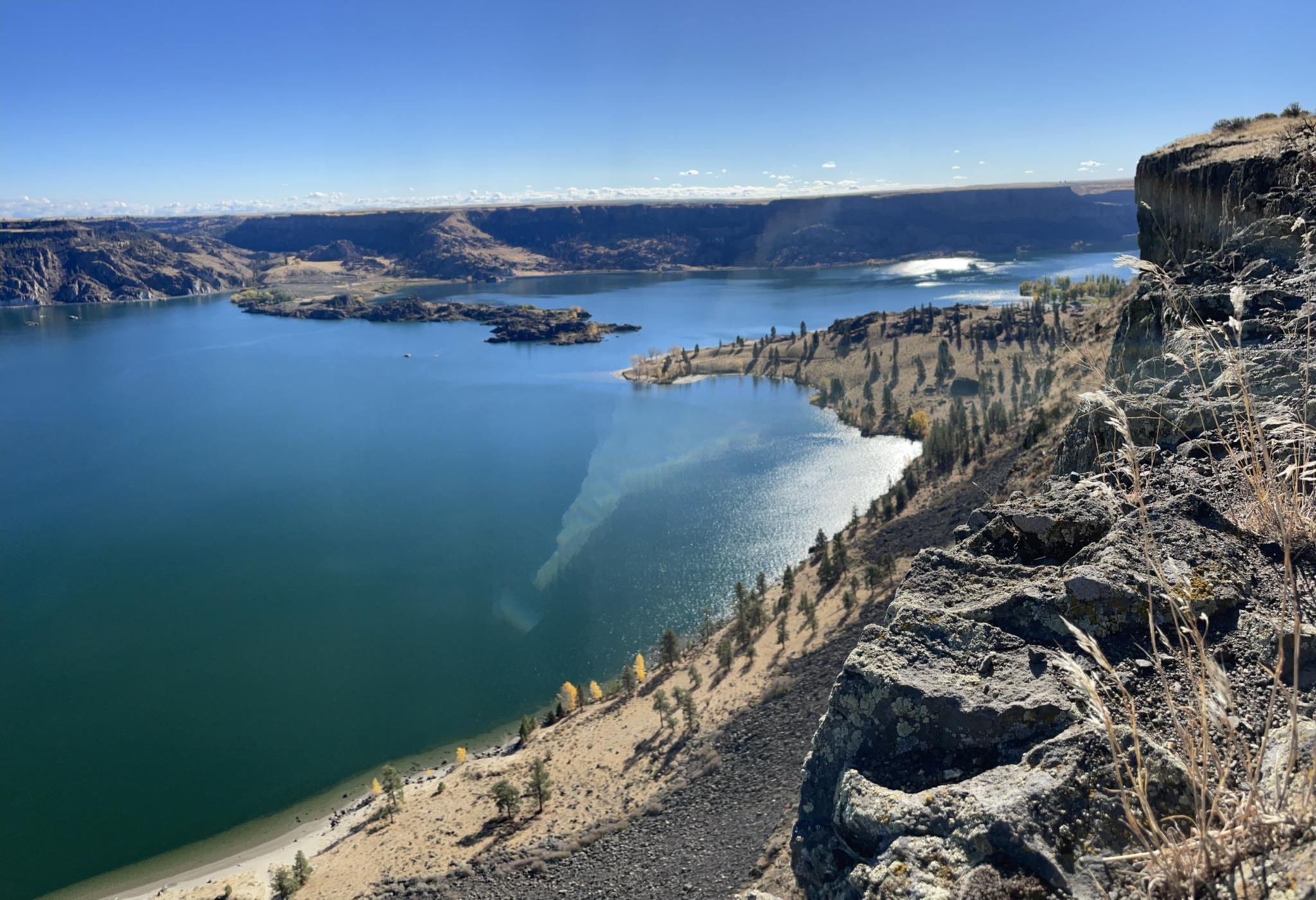 A vast blue lake with islands and rocky shores under a bright, clear sky.