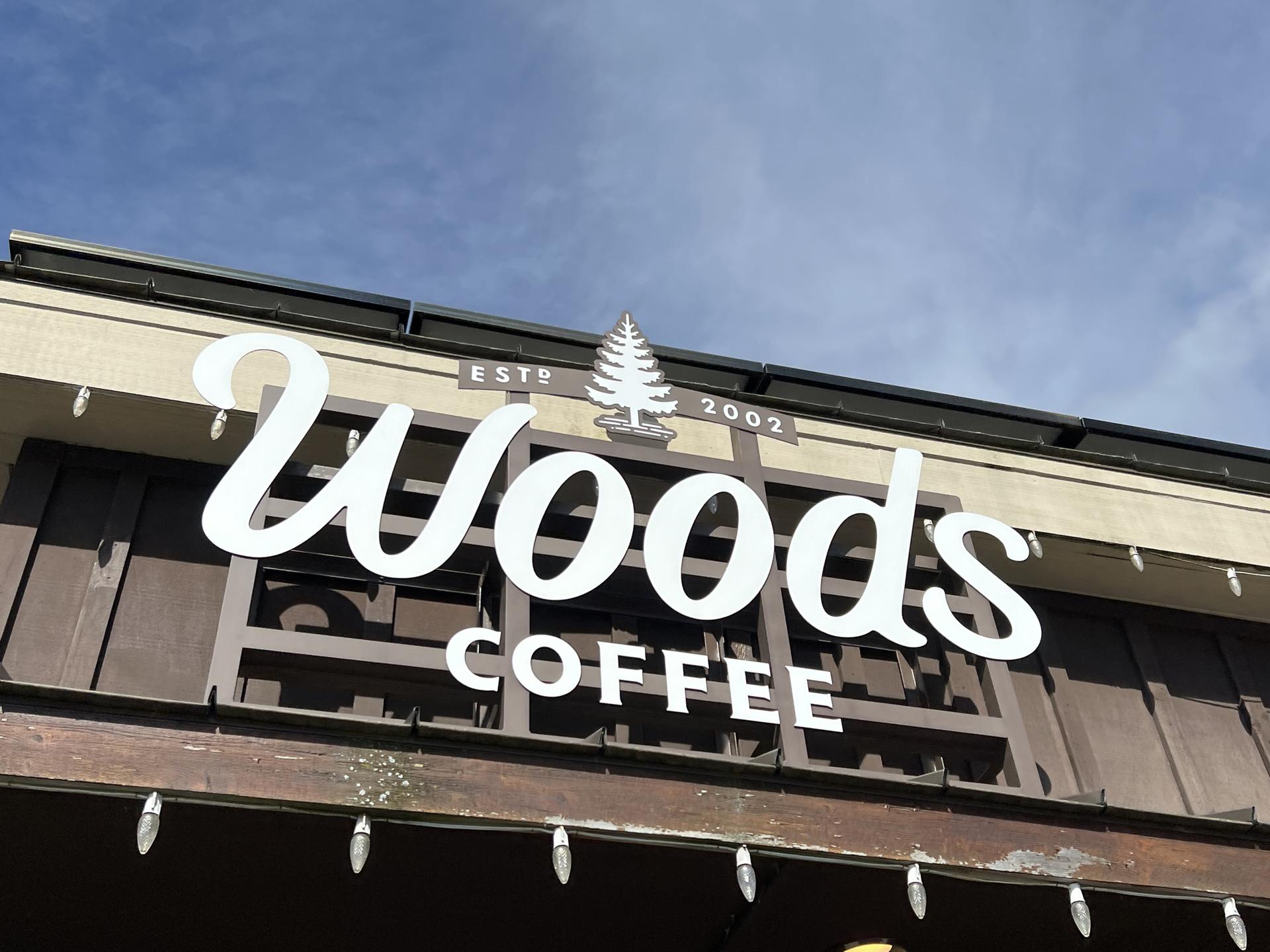 Close-up of a "Woods Coffee" sign with a tree logo on a building.