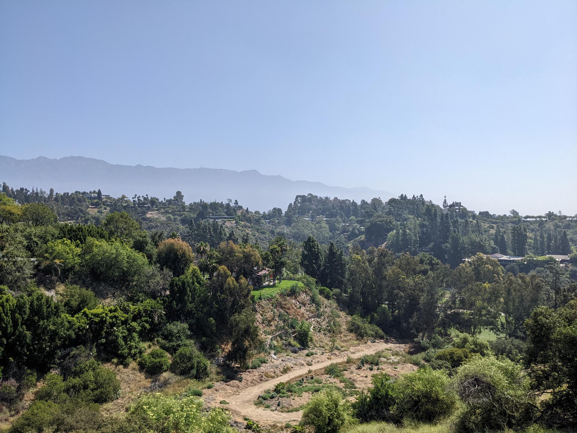 Verdant hills and a winding dirt path under a clear, bright sky.