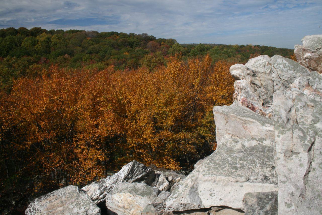 Rocky outcrop overlooking a forest with vibrant autumn foliage under a cloudy sky.