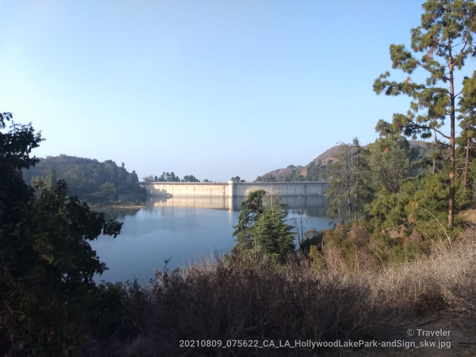 Wide view of a large dam wall spanning a calm body of water.
