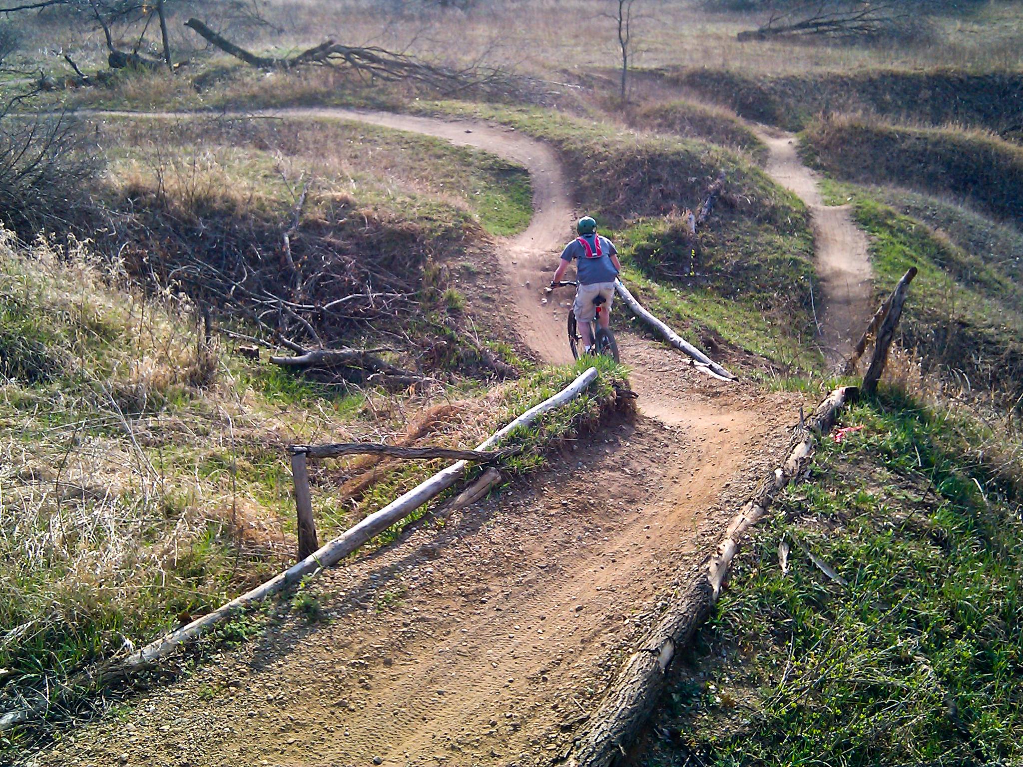 Person mountain biking on a winding dirt trail through grassy hills.