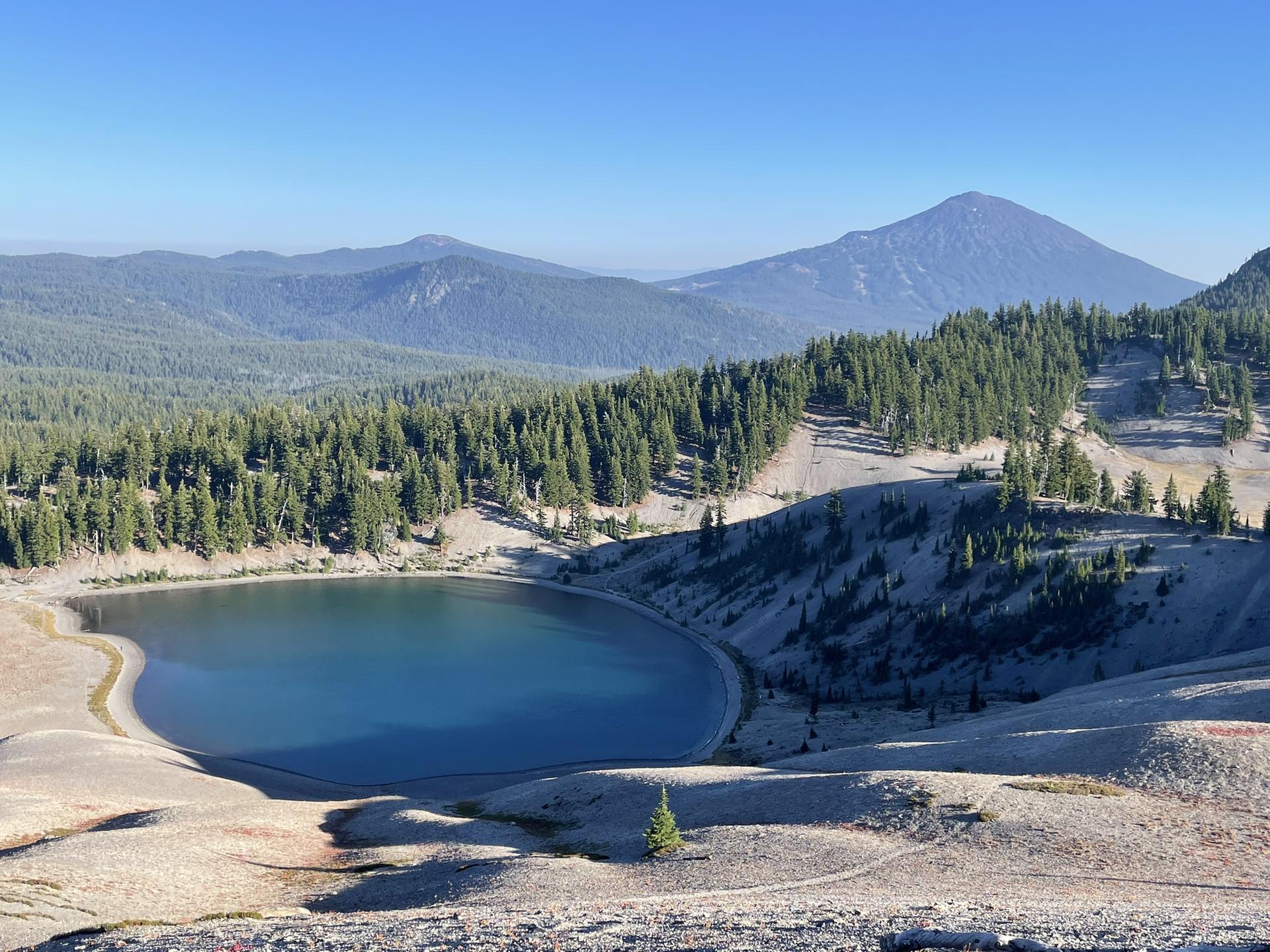 A serene blue lake surrounded by forested slopes and a prominent distant mountain.