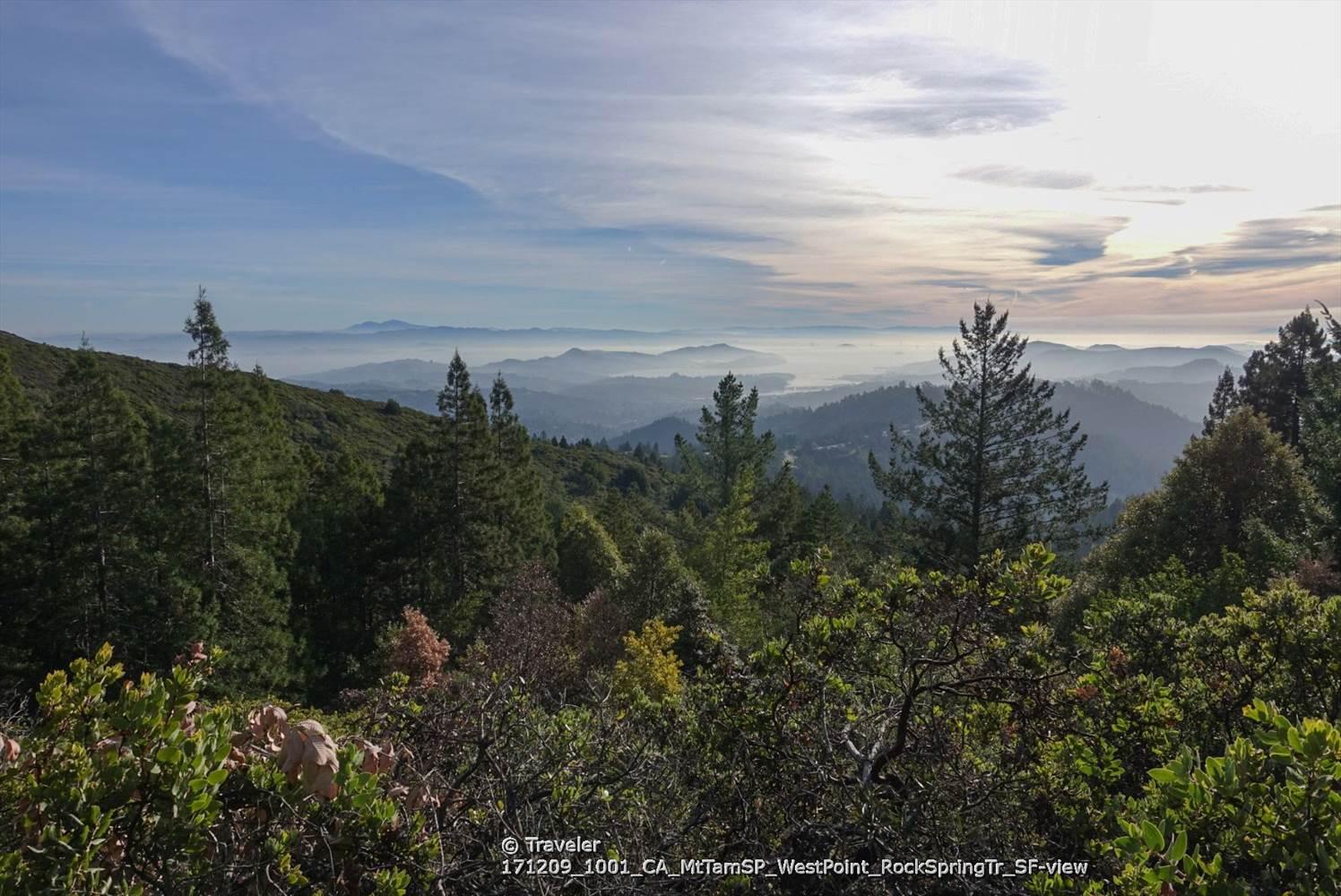 Panoramic view of forested mountains and hazy valleys under a bright sky.