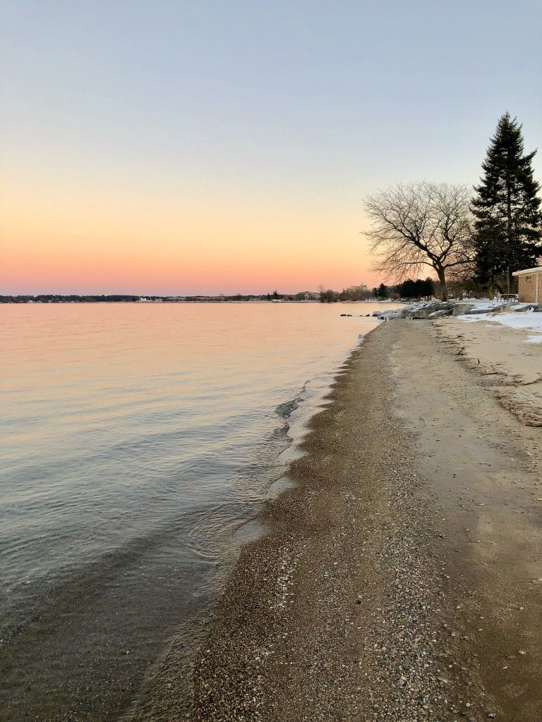 Serene shoreline at sunset with calm water, sand, and distant trees. - Traverse City – Boardman Lake Trail loop from Traverse City