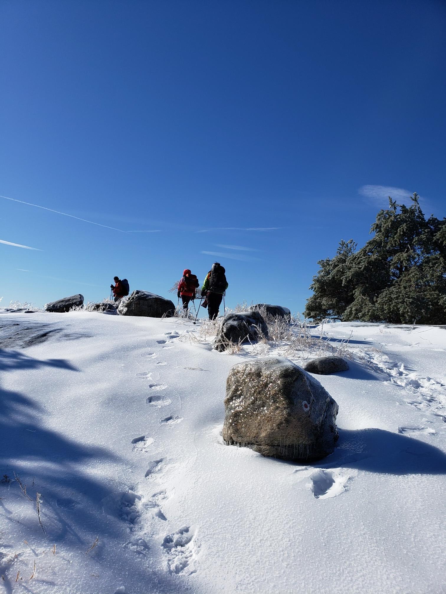 Three hikers on a snowy, rocky hill under a clear blue sky.