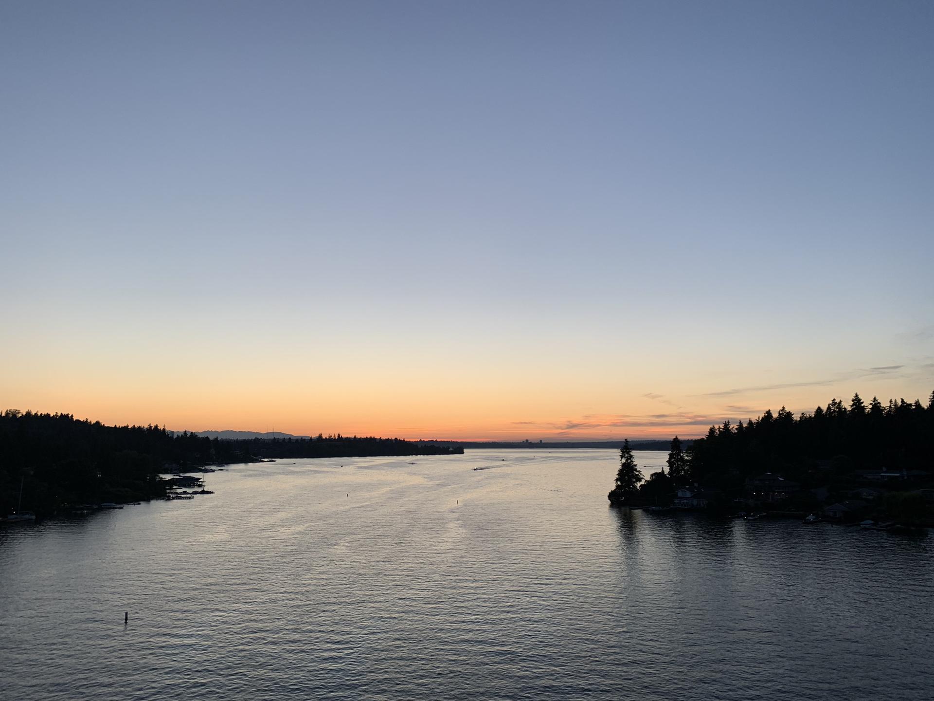 Serene sunset over a wide body of water with forested shores.