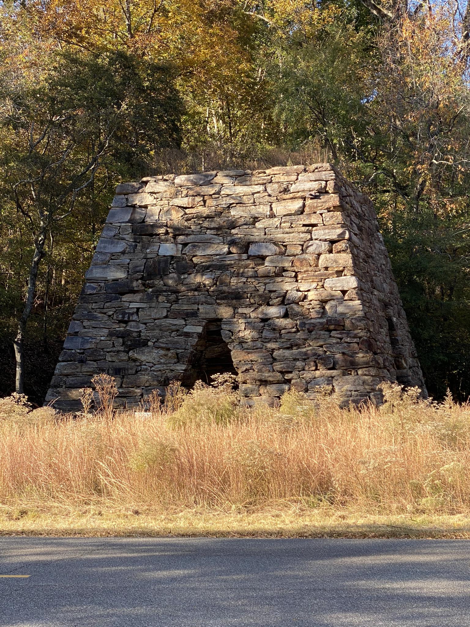 Large, ancient-looking stone structure in a grassy field with autumn trees.