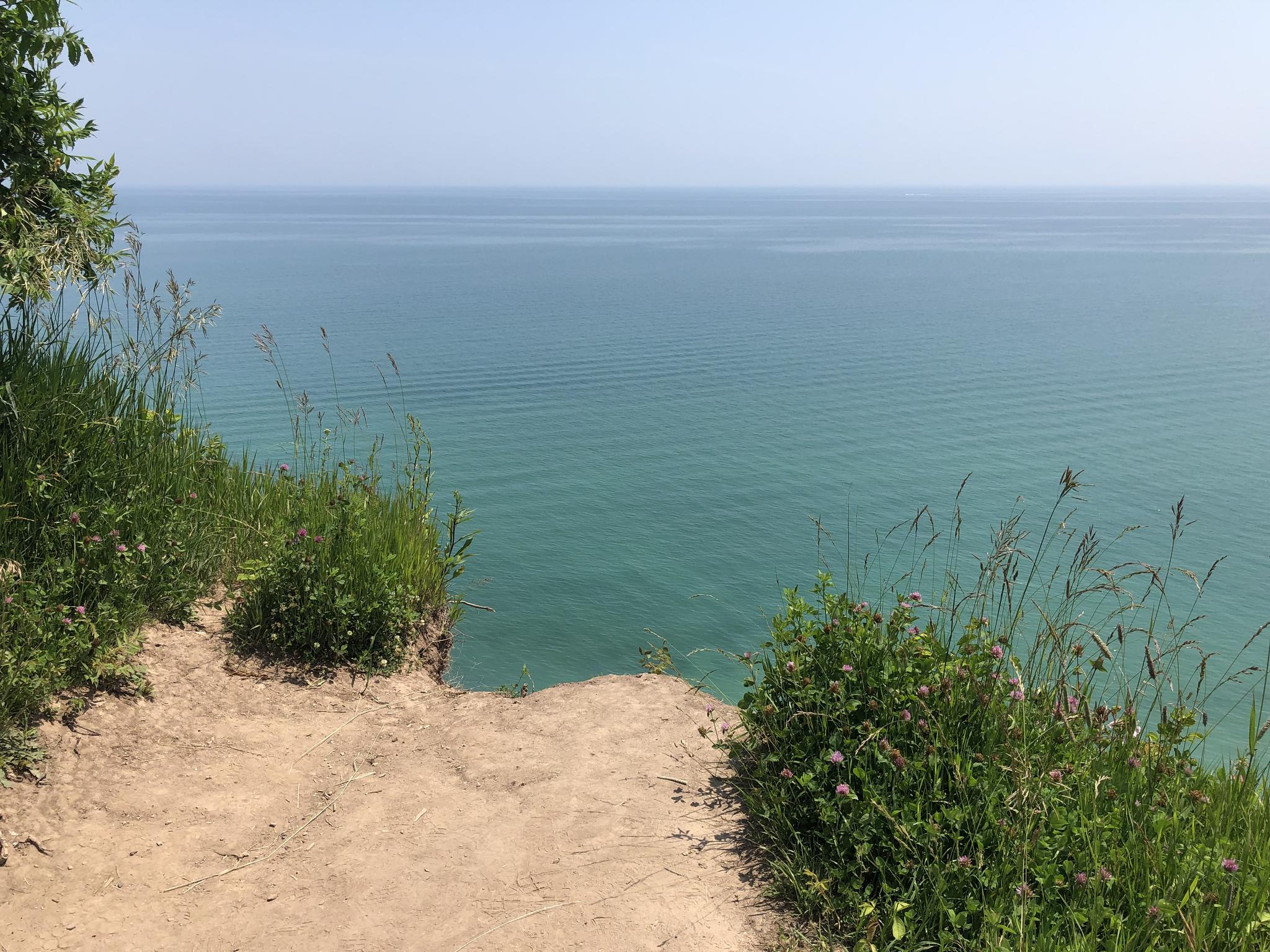 Bright sunny view of turquoise water from a sandy cliff edge.