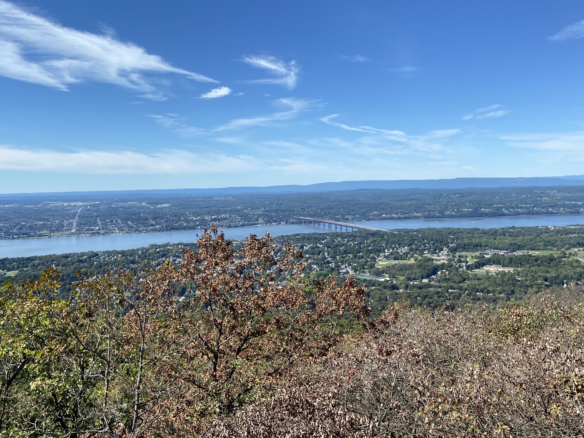 An expansive view of a wide river, distant bridge, and forested landscape. - Overlook Trail
