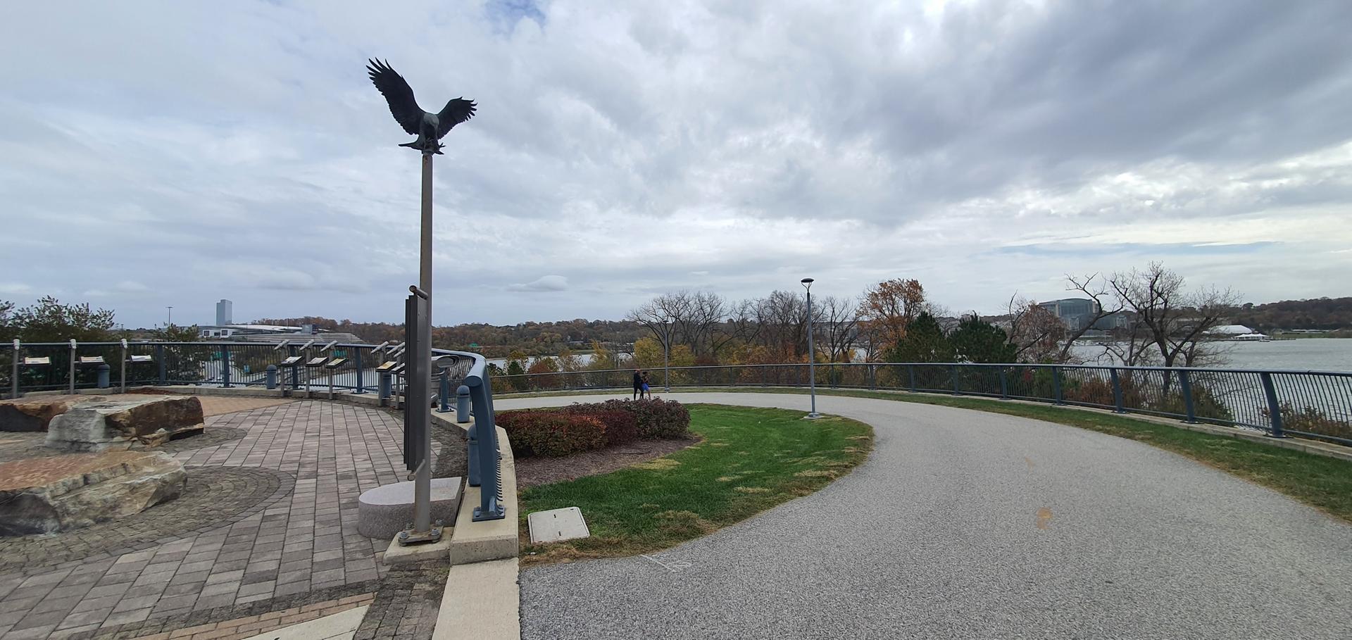 Eagle statue on a paved overlook with a distant river and trees.