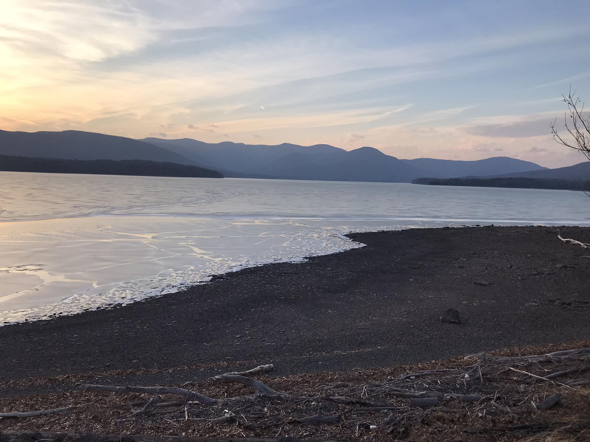 Partially frozen lake at dusk, with dark shore and distant mountains.