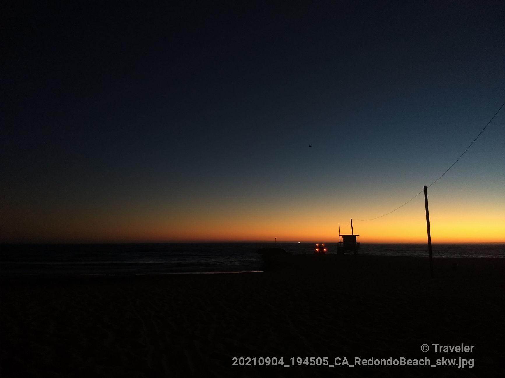 A dark beach at twilight with a lifeguard tower silhouette and orange horizon.