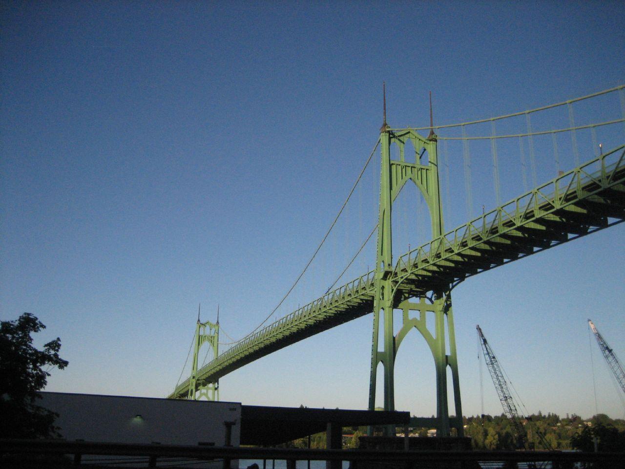Massive green suspension bridge spans across a clear blue sky.