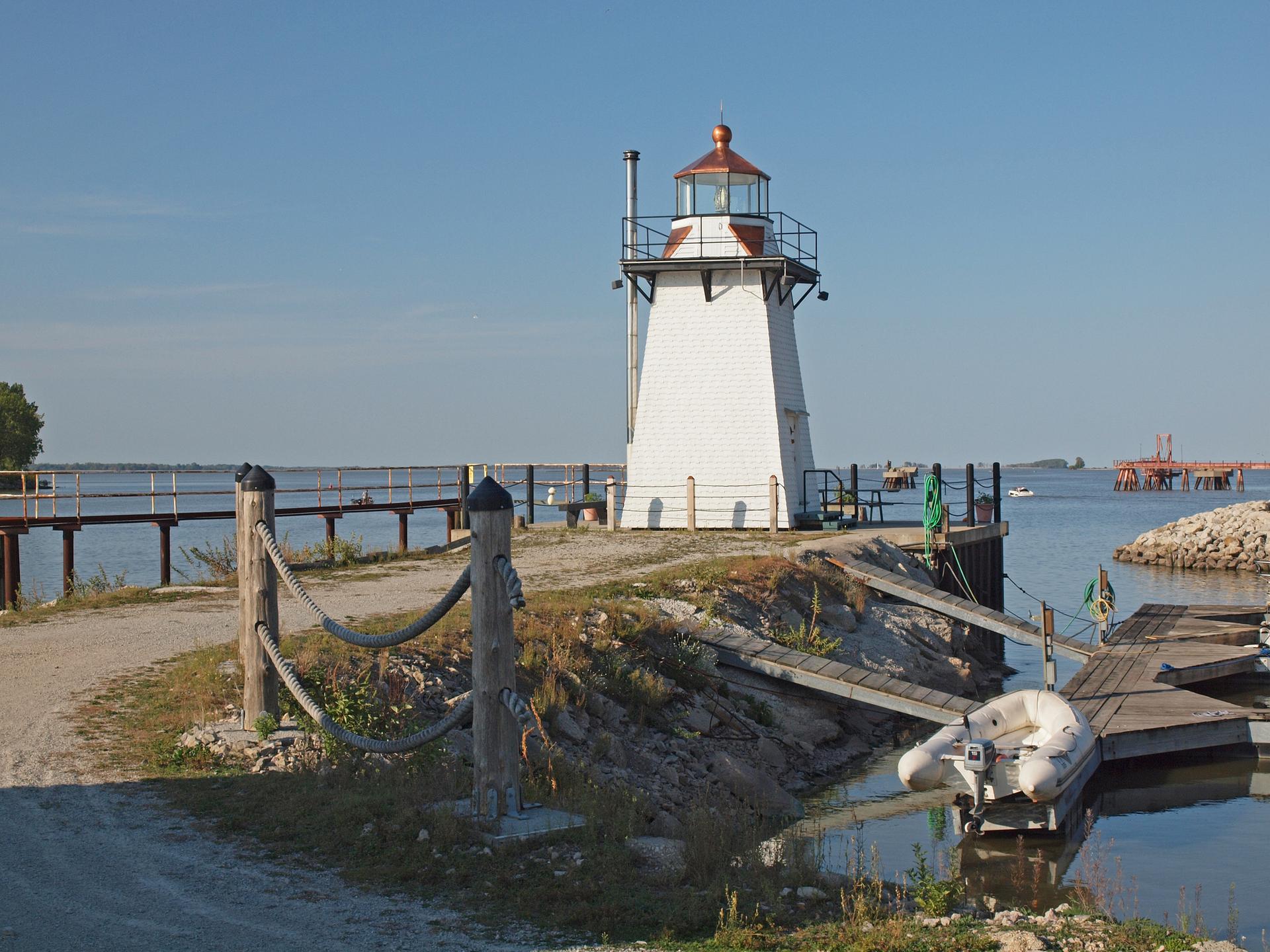 White lighthouse on a sunny day overlooking water with docks.