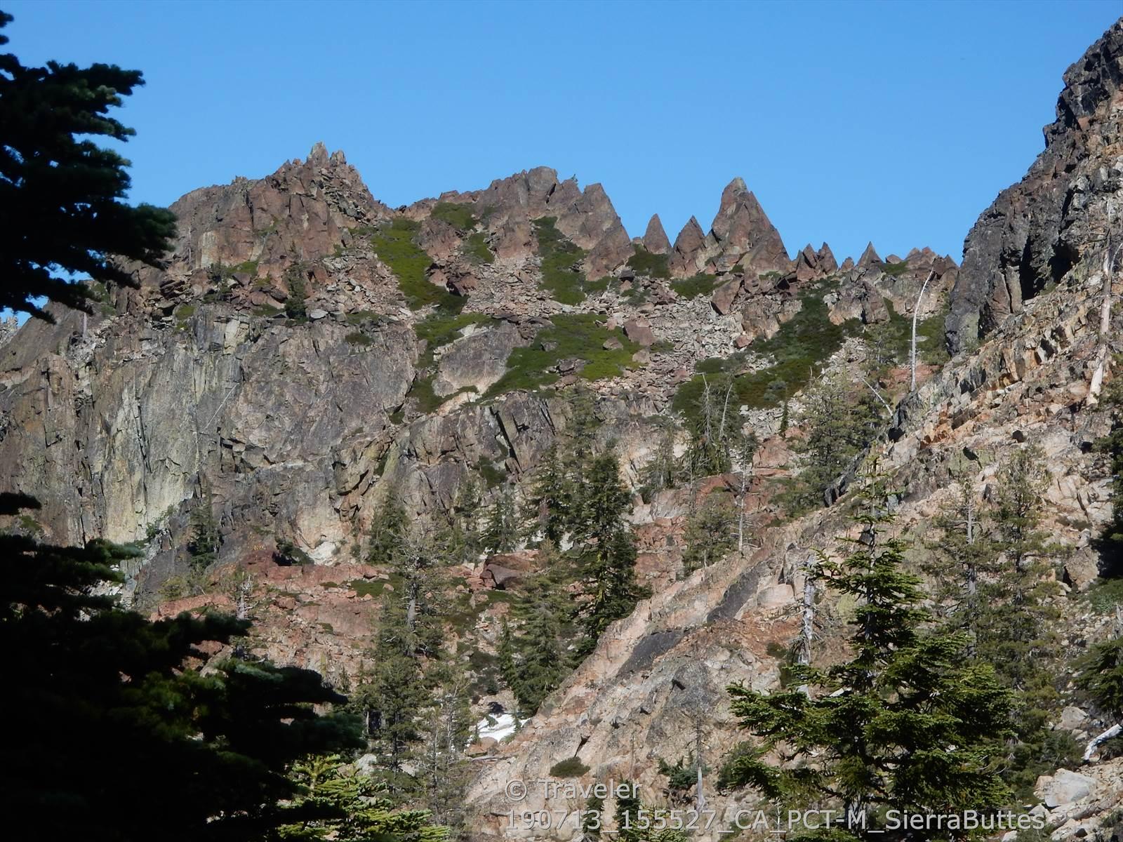 Rugged, rocky mountain peaks with sparse trees under a clear sky.