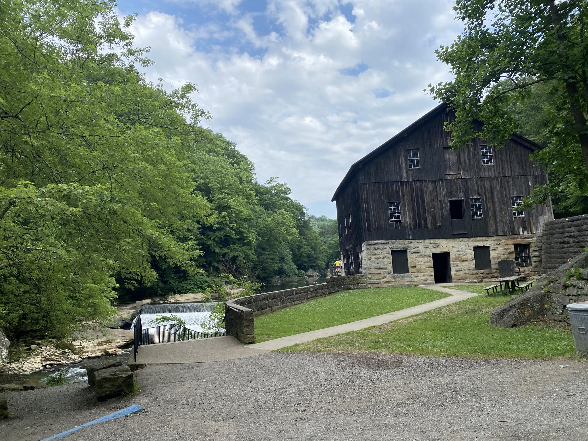 An old wooden mill building stands beside a river with a small waterfall.