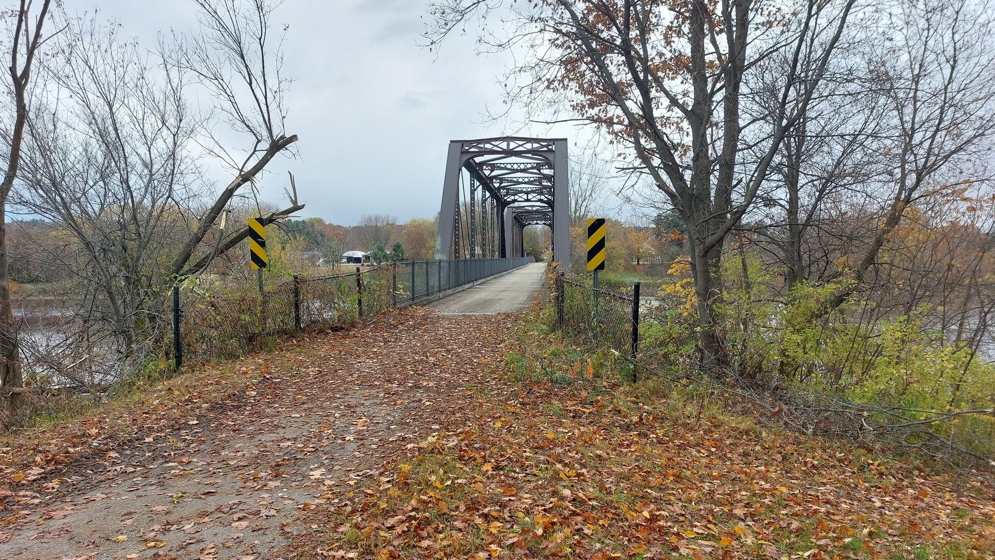 Overcast view of a metal truss bridge over water, surrounded by autumn trees.