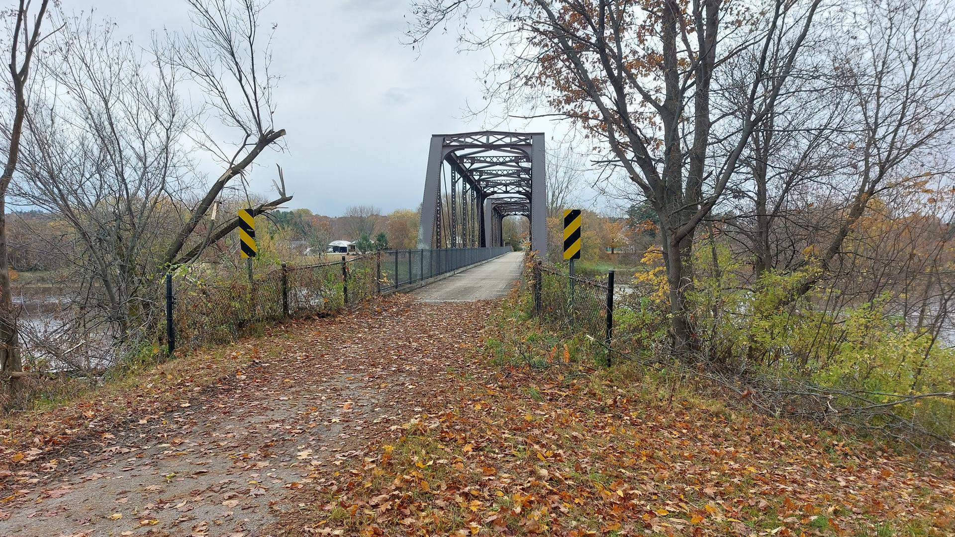 Overcast view of a metal truss bridge over water, surrounded by autumn trees.