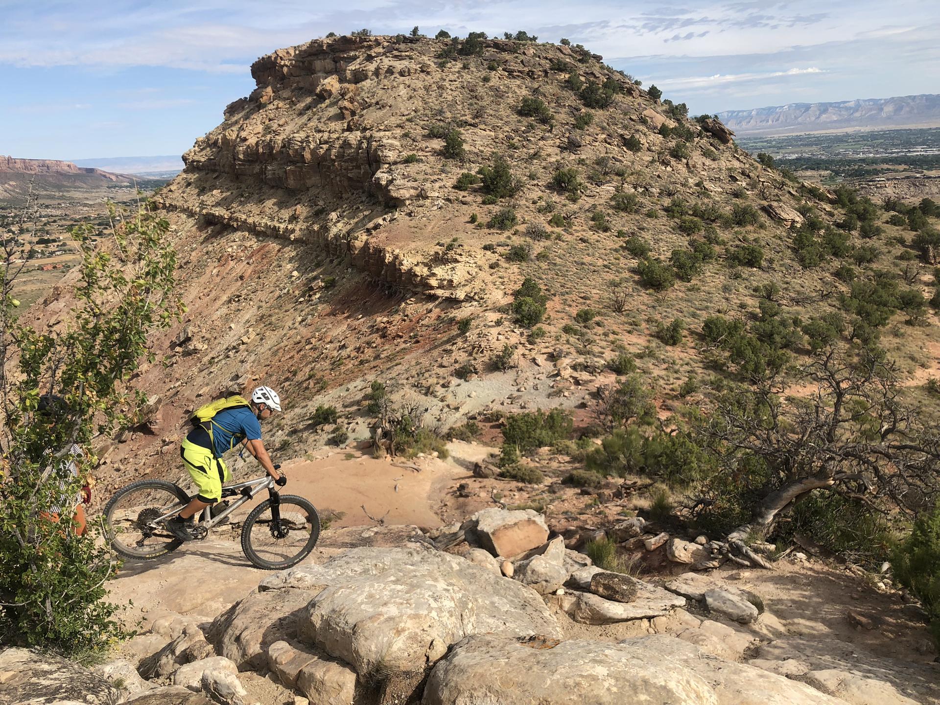 Mountain biker on a rocky trail with a large, layered desert mesa.