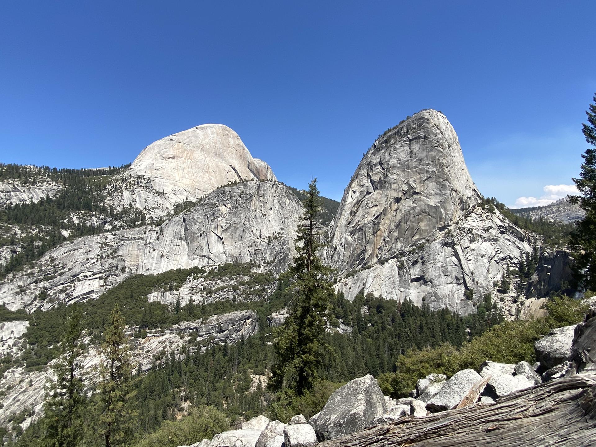 Two massive granite mountains rise above a pine forest under a clear blue sky.