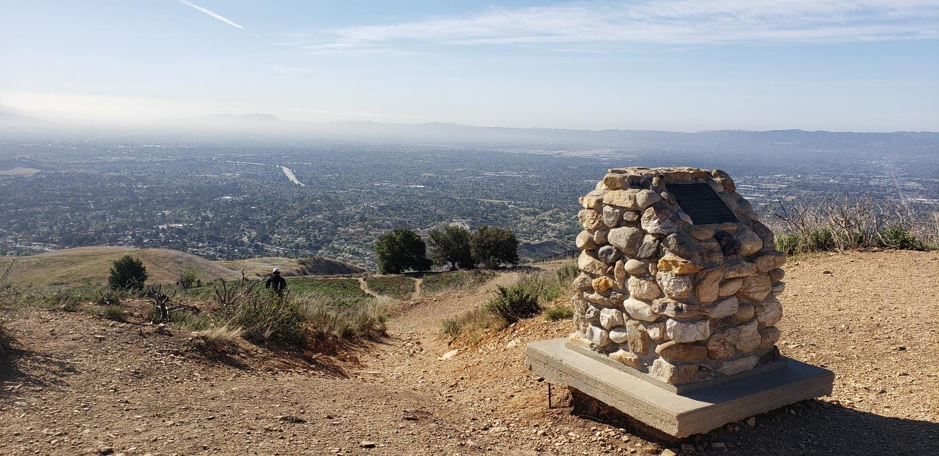 Stone monument on a sunny hill overlooking a vast city.