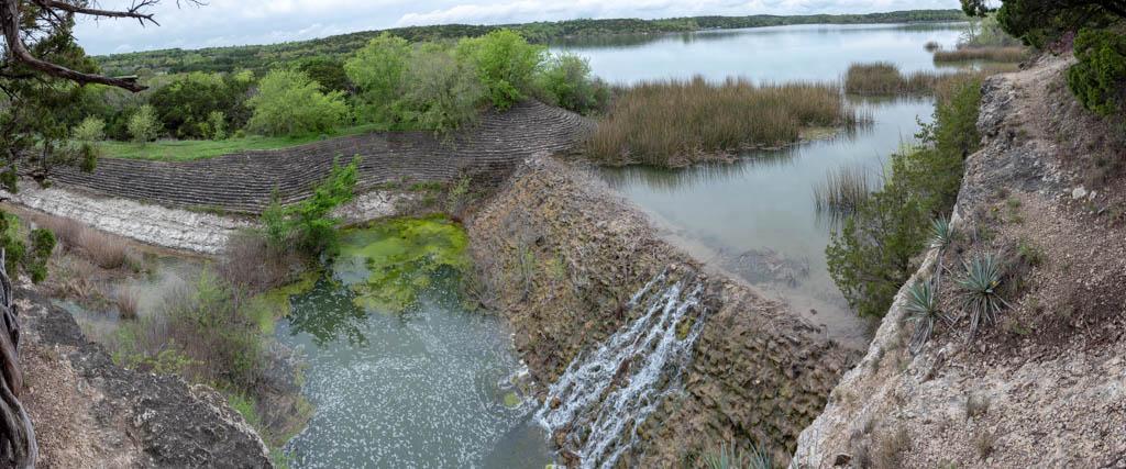 Panoramic view of a waterfall cascading into a lake surrounded by lush greenery.