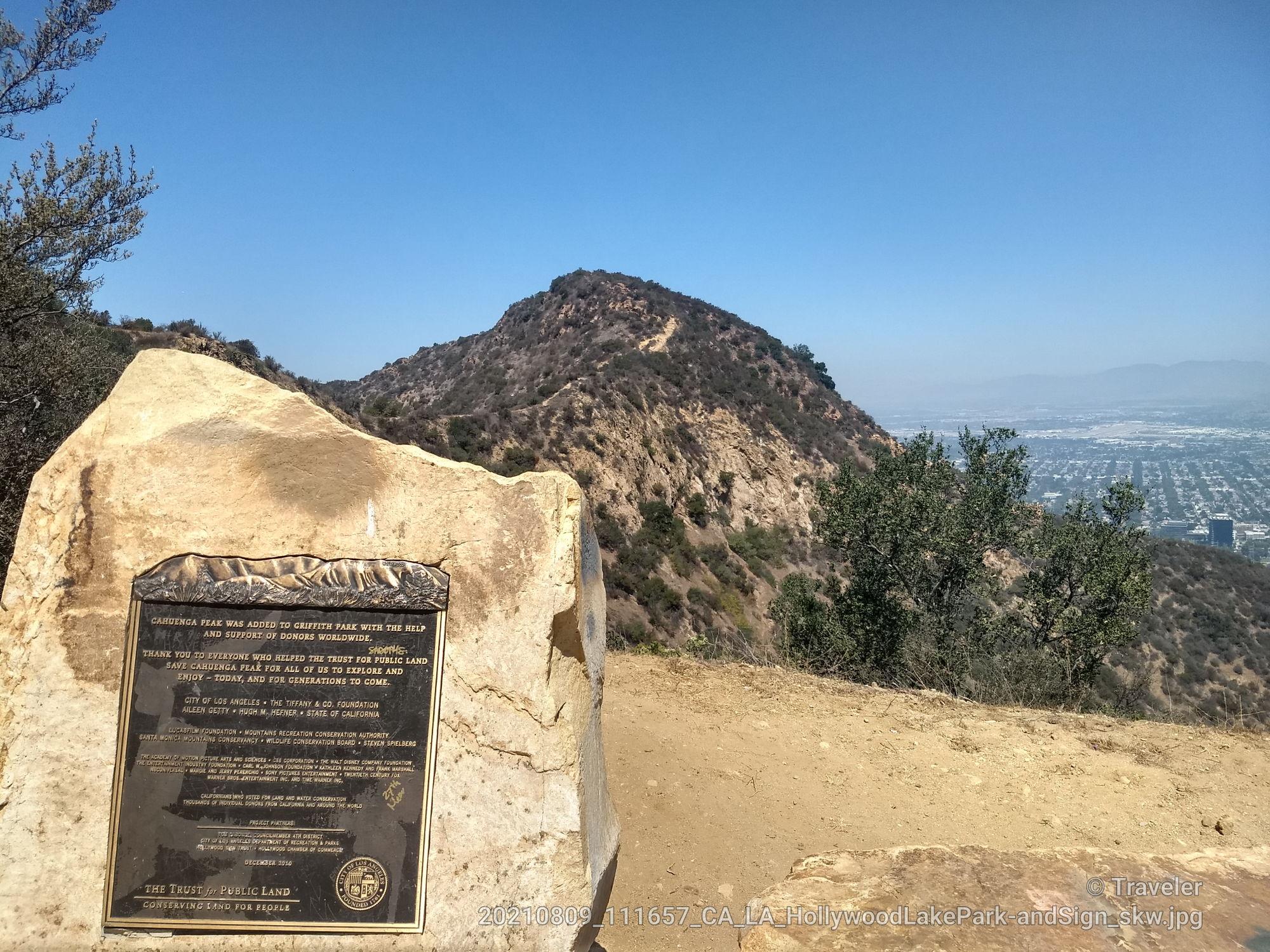 A stone monument with a plaque stands before a distant city and hills.