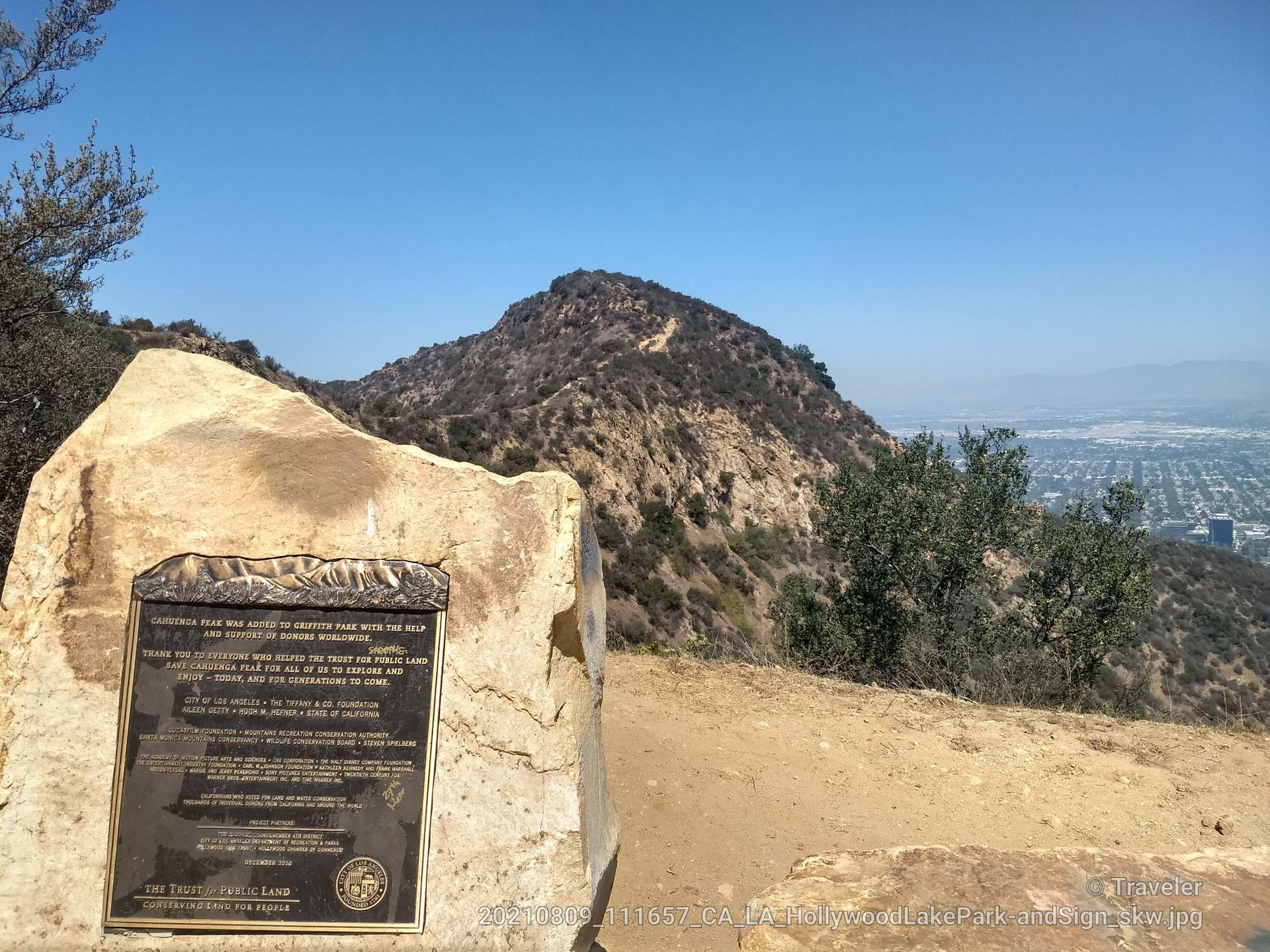 A stone monument with a plaque stands before a distant city and hills.