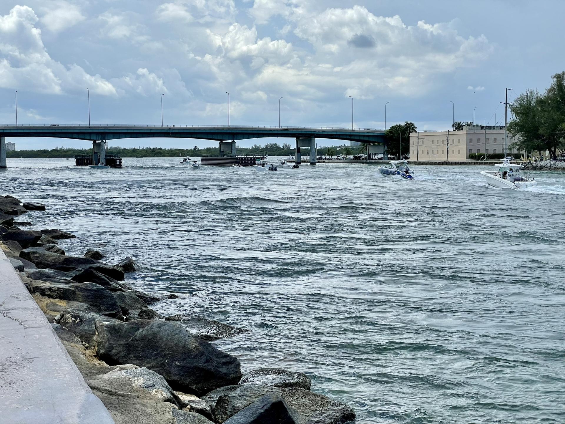 Boats on a waterway under a large bridge on a cloudy day.