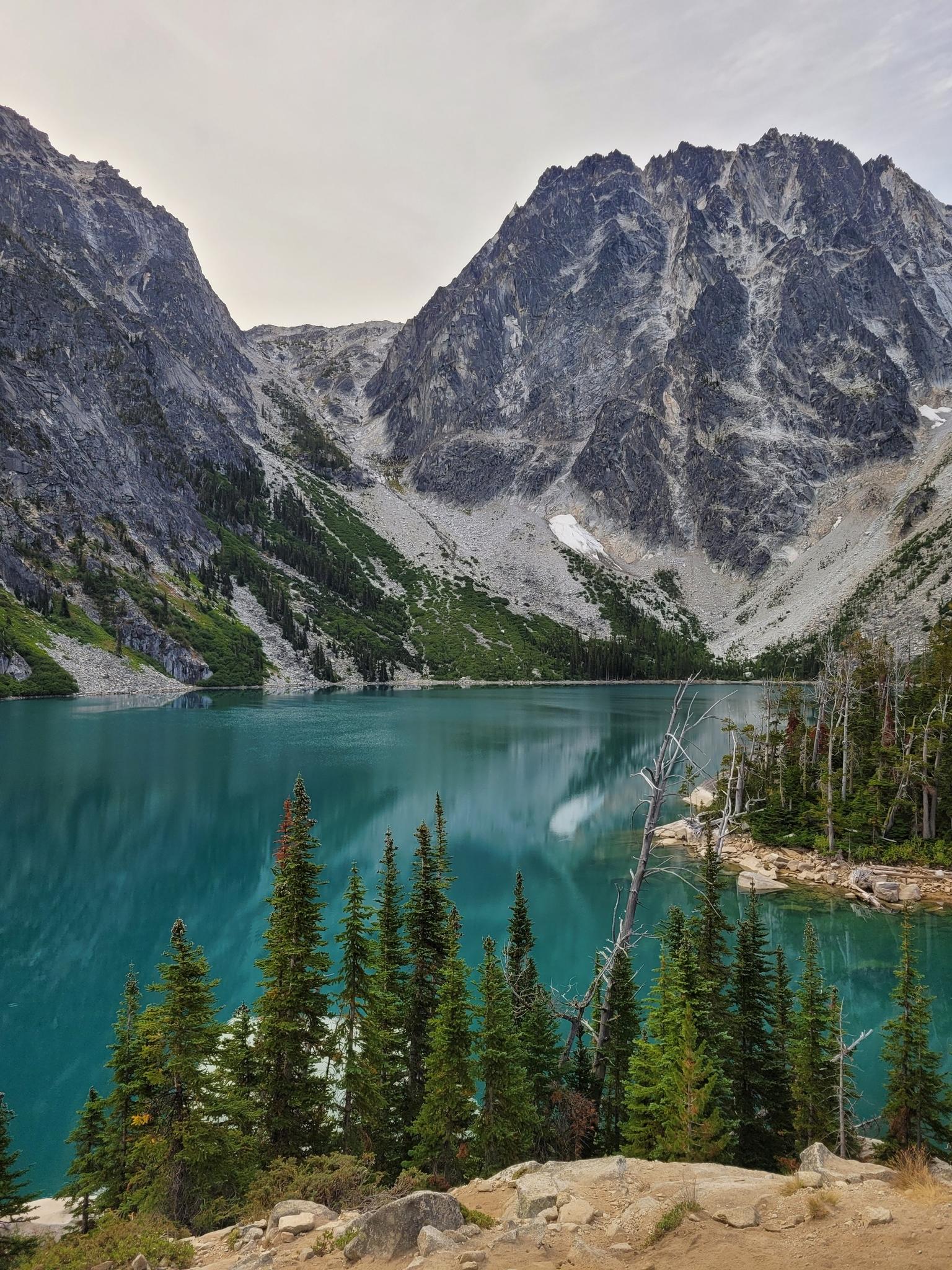 Turquoise alpine lake surrounded by steep, rugged mountains and evergreen trees.