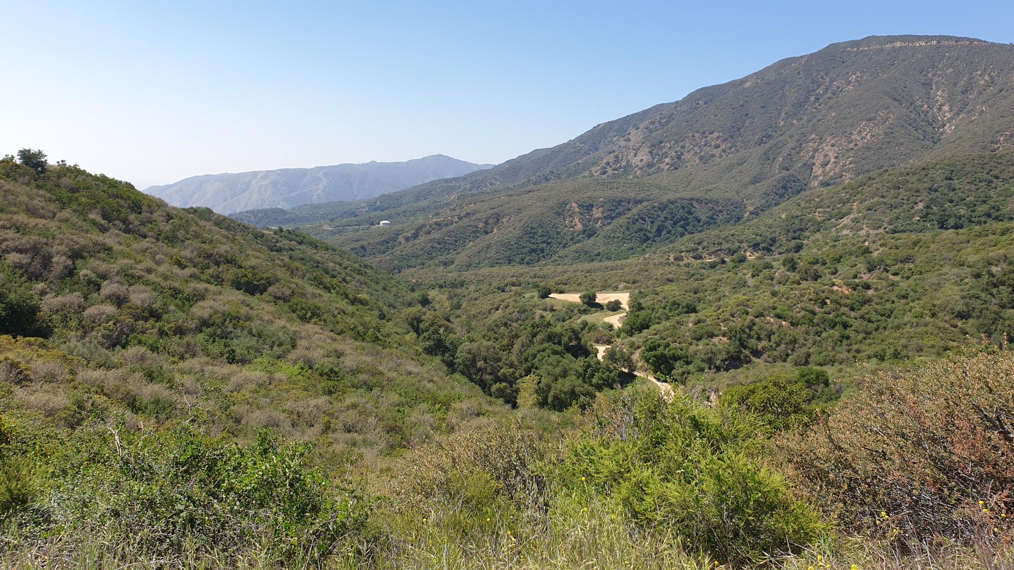 Wide green valley with a winding dirt road and distant mountains.