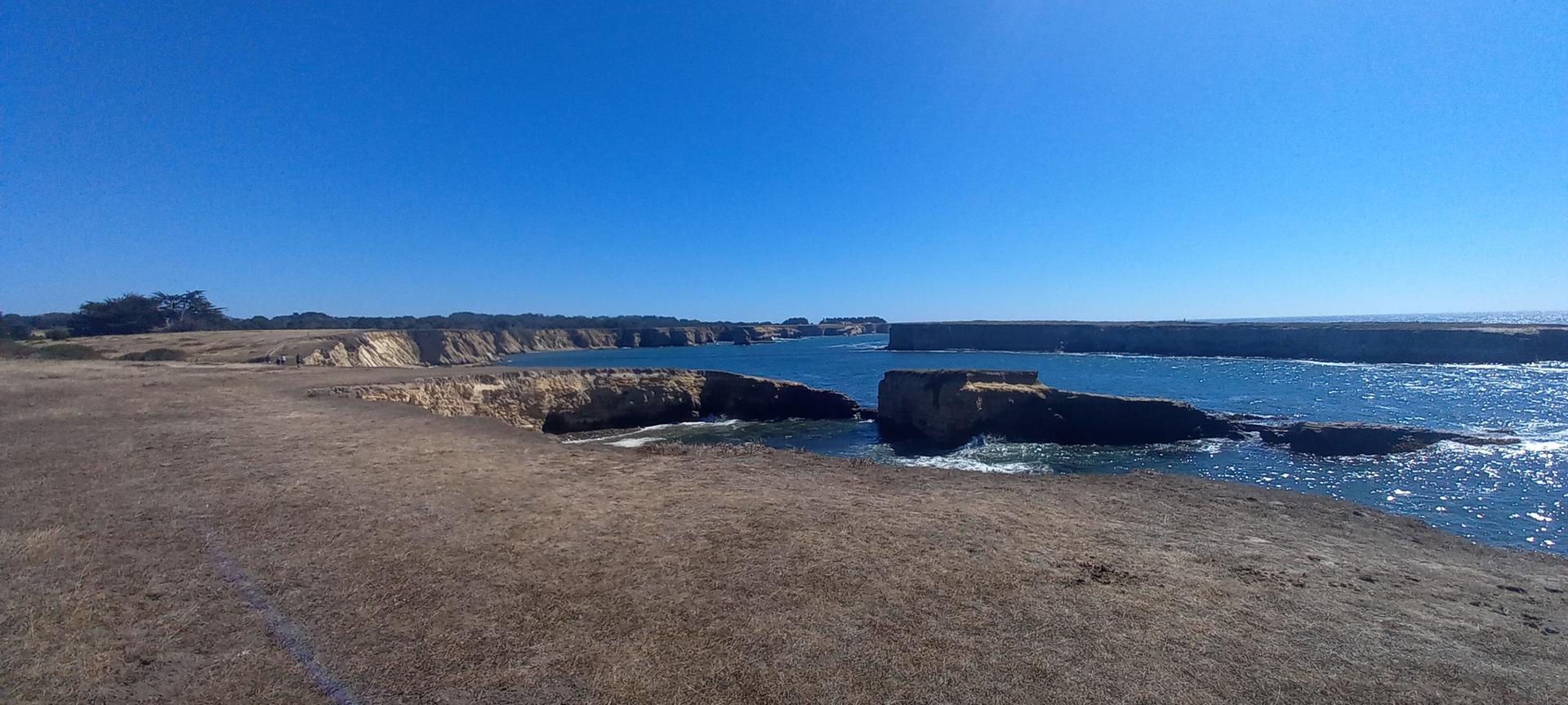 Panoramic view of dry grassy cliffs overlooking a bright blue ocean.