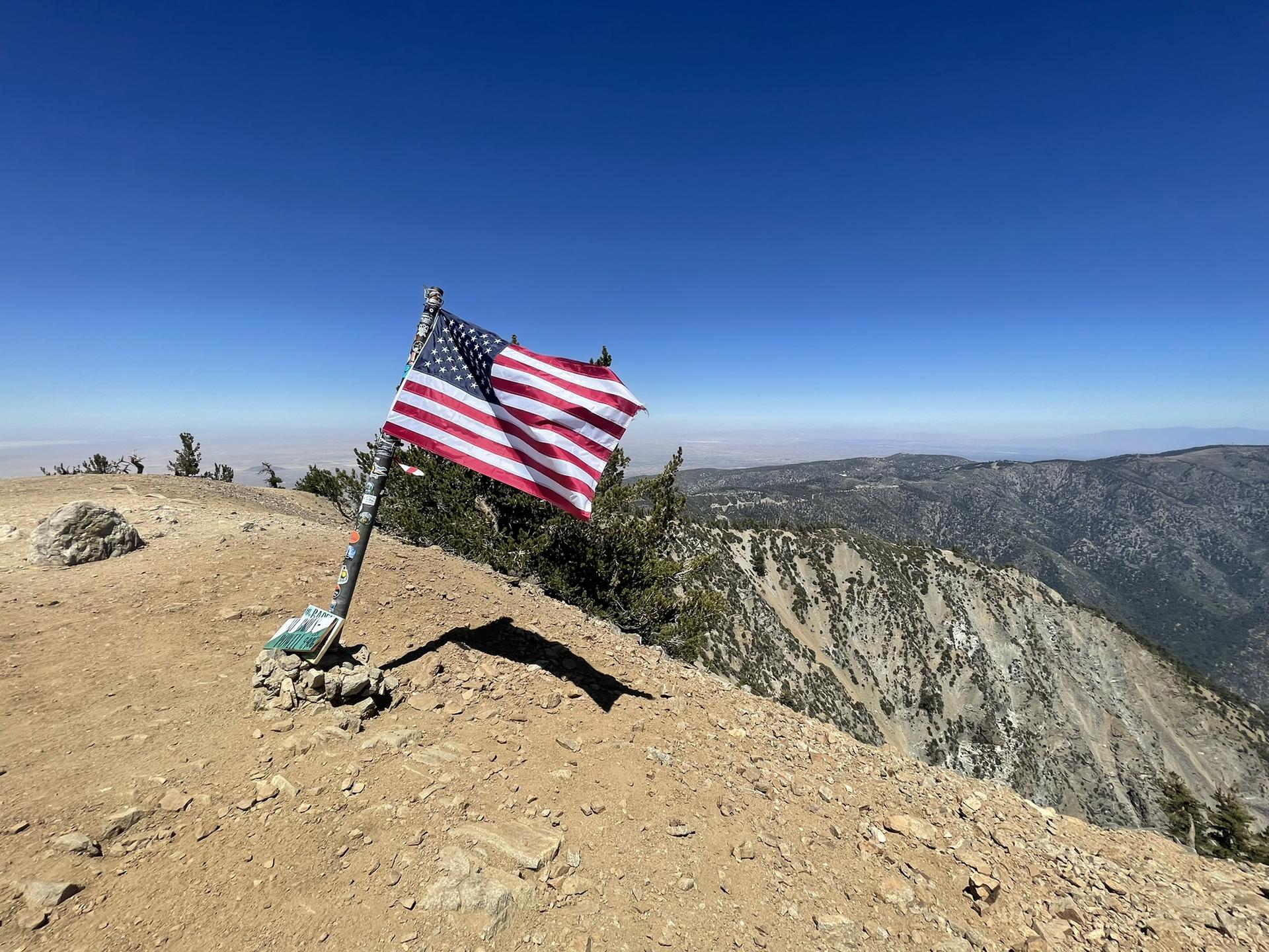 American flag on a pole on a rocky mountain peak overlooking valleys.