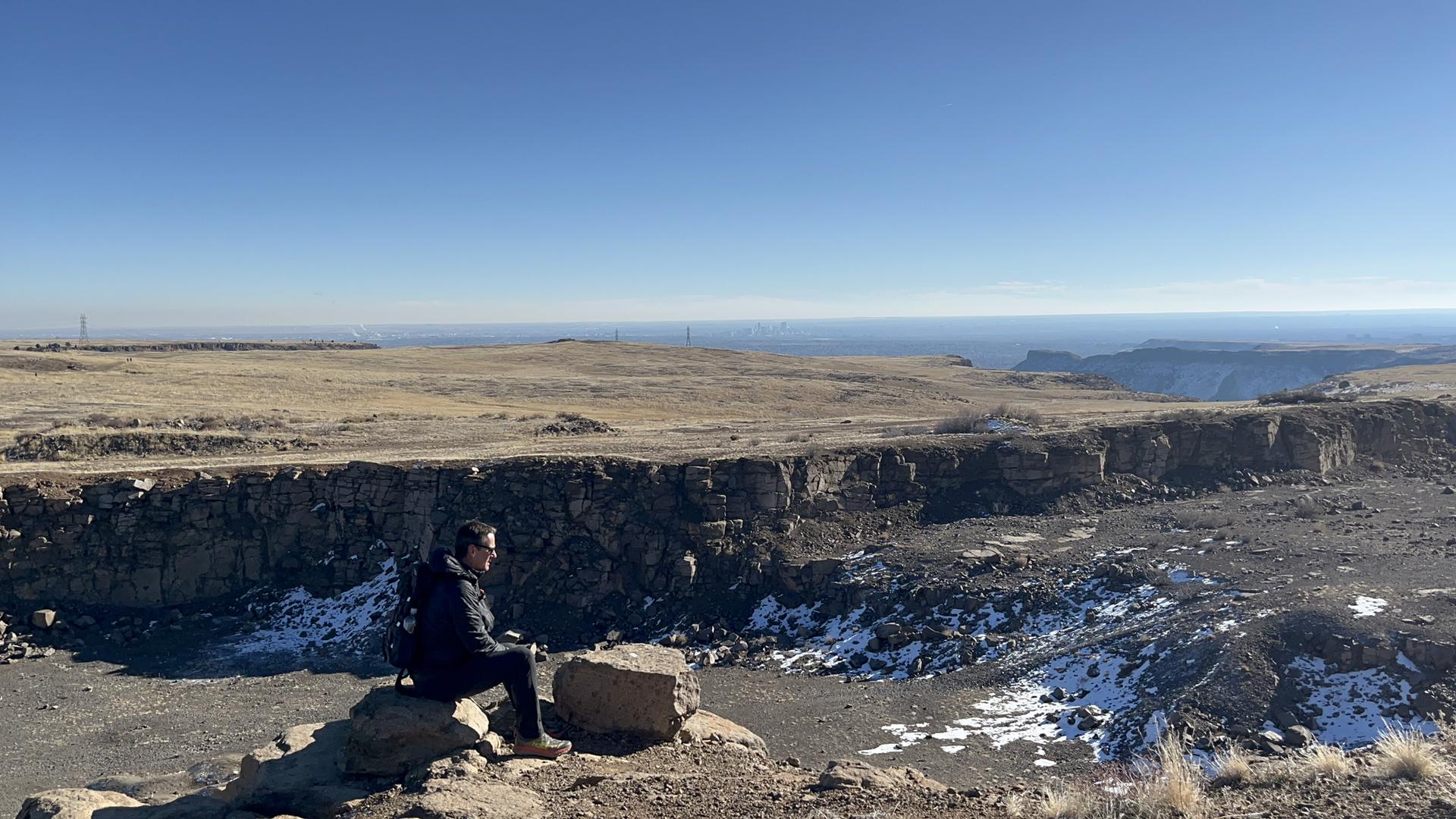 Person sits on a rock overlooking a vast canyon with patches of snow.
