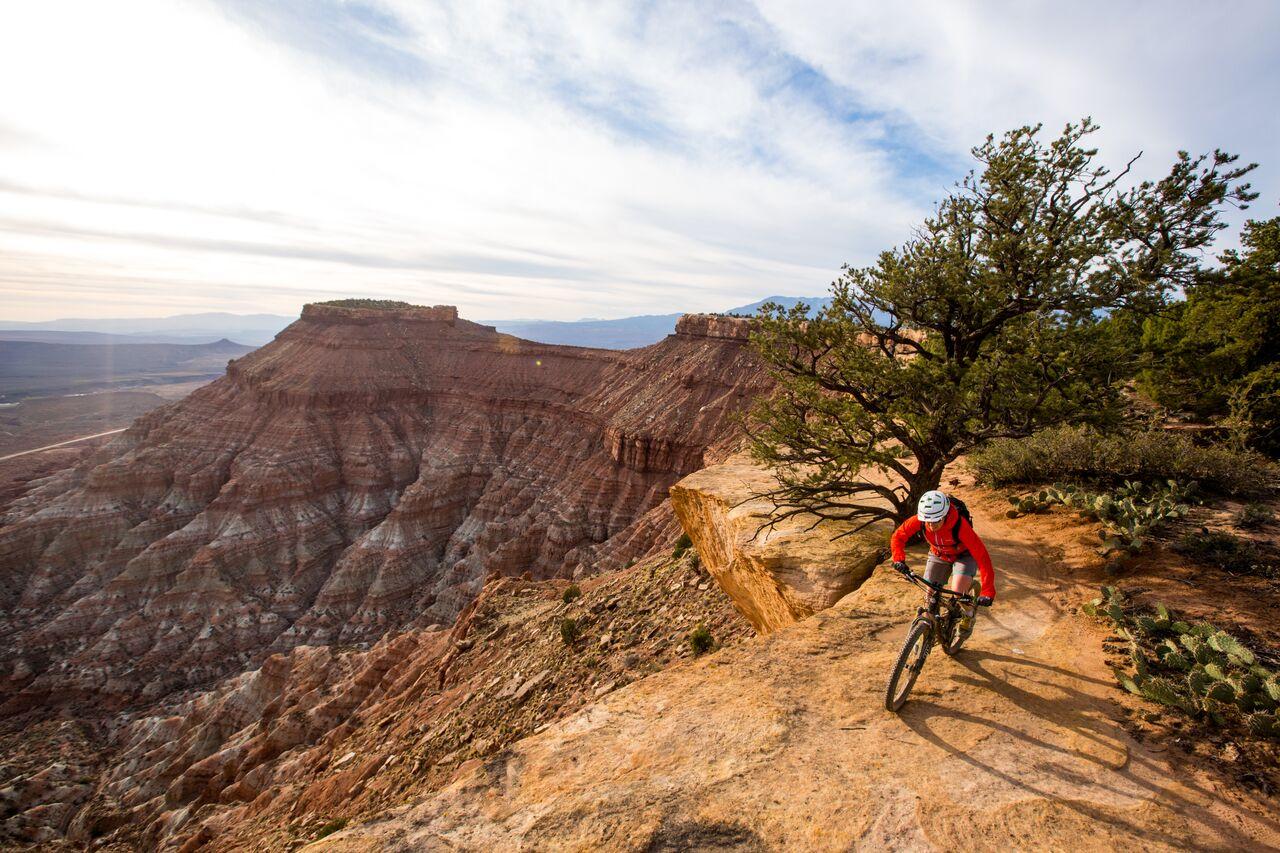 Mountain biker rides along a red rock cliff edge at golden hour.