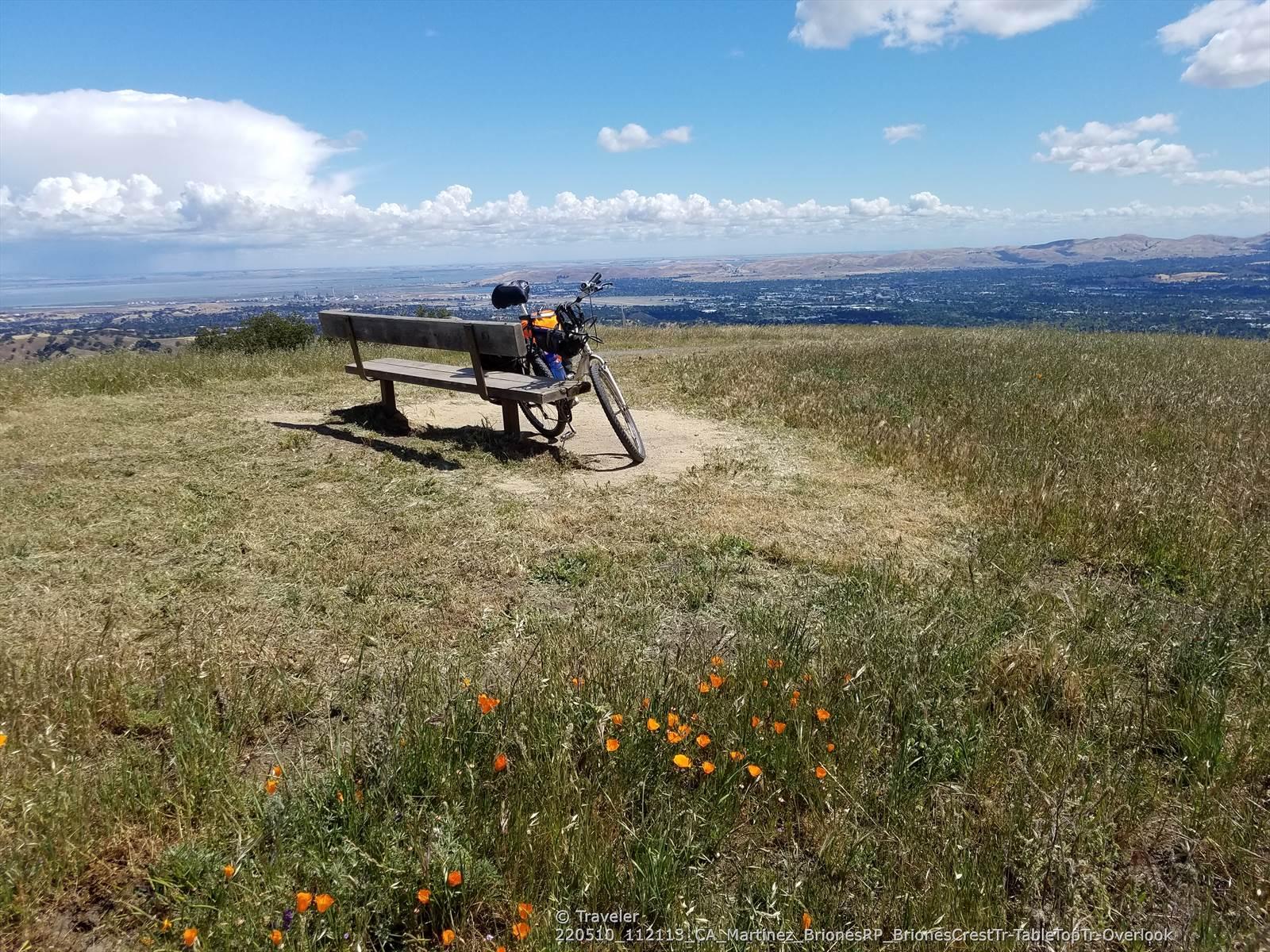 Bicycle parked next to a bench on a grassy hill overlooking a valley.