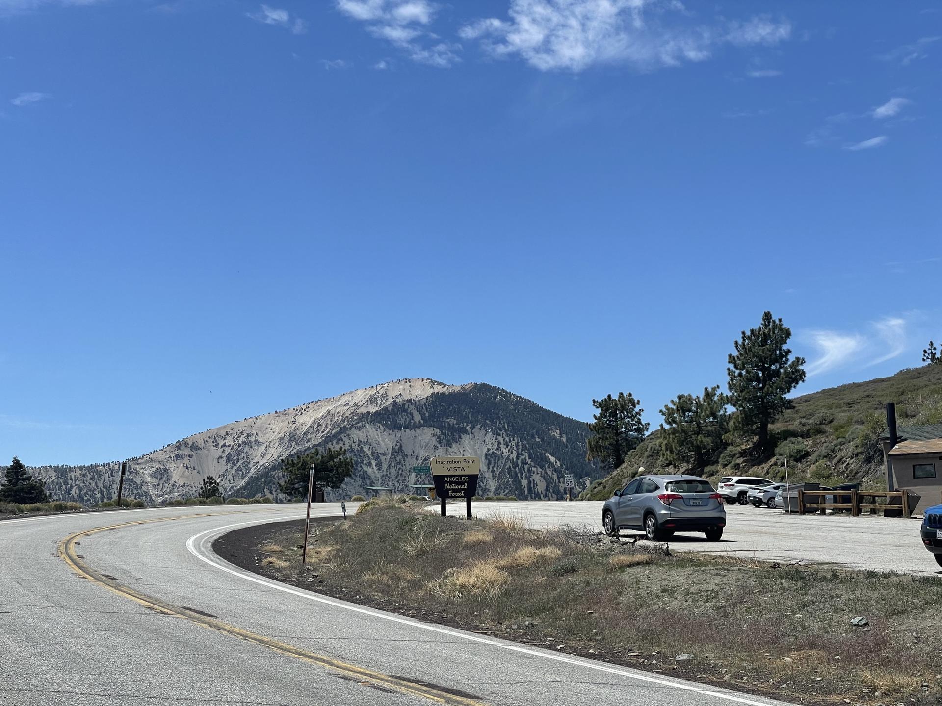 Winding road leading to a parking area with a large mountain in the background.