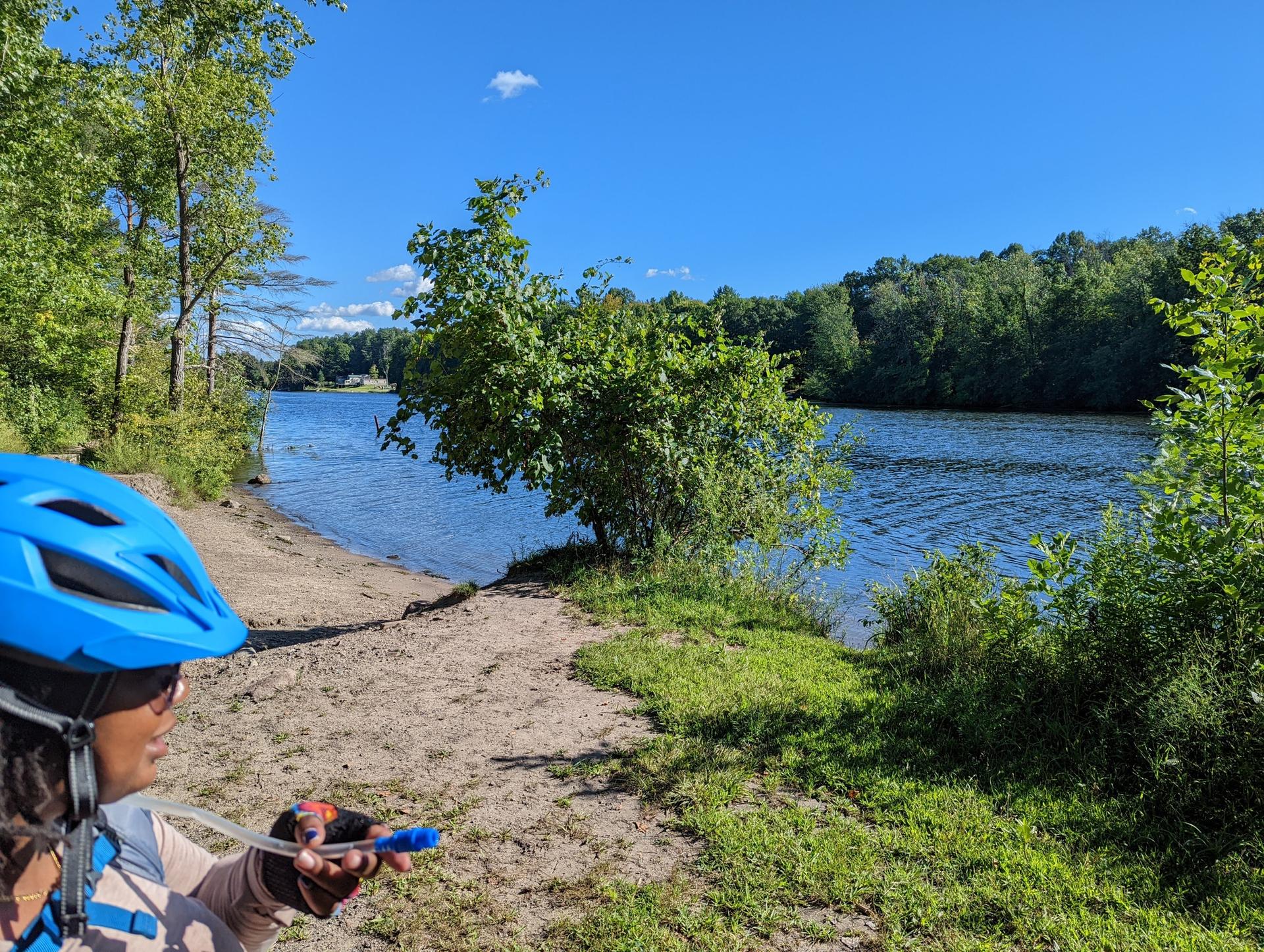 Person in blue helmet by a sunny river with green trees.