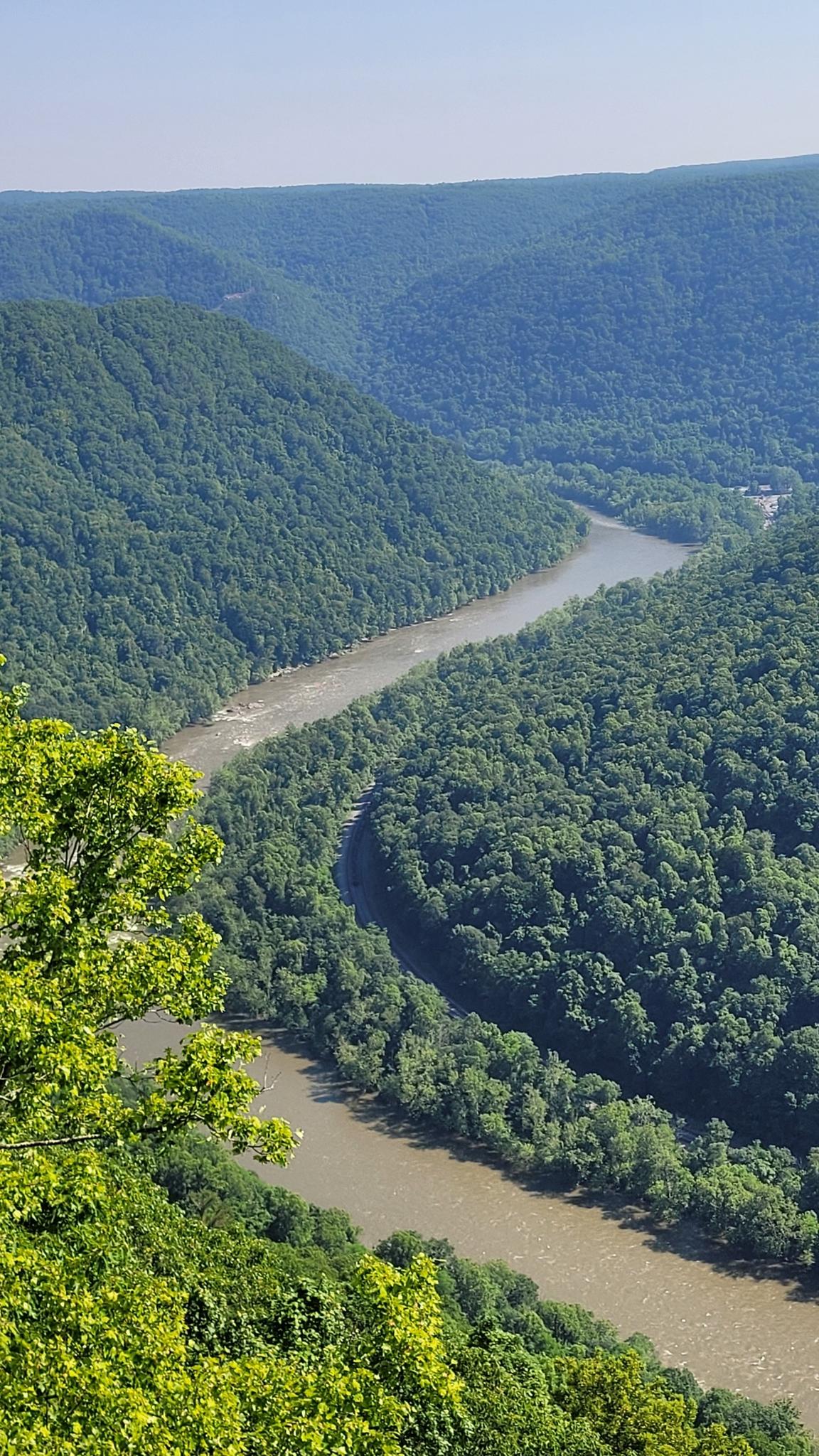 A wide river snakes through a lush green valley on a bright day.