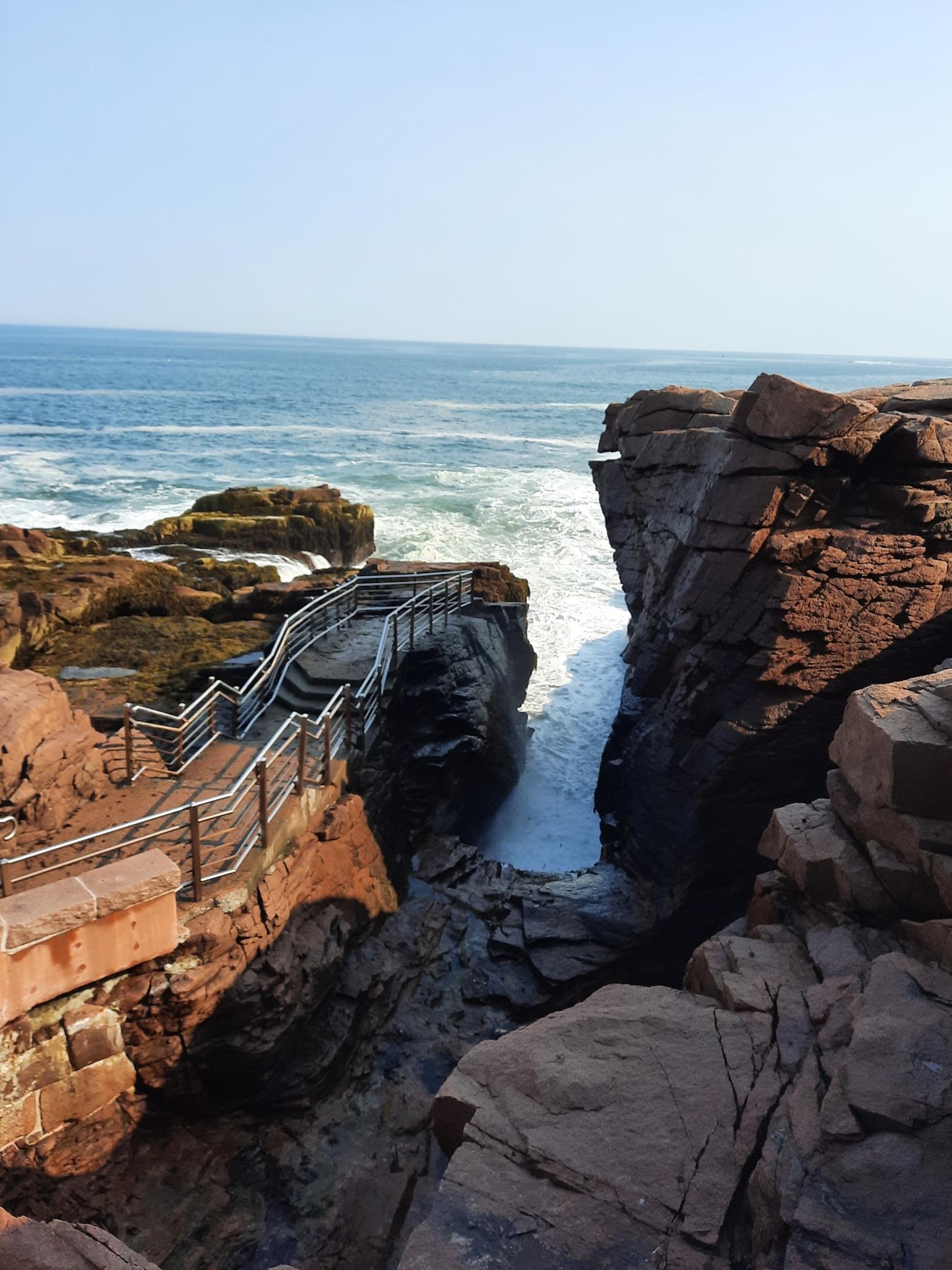 Steep metal stairs descending into a rocky ocean cove with crashing waves.