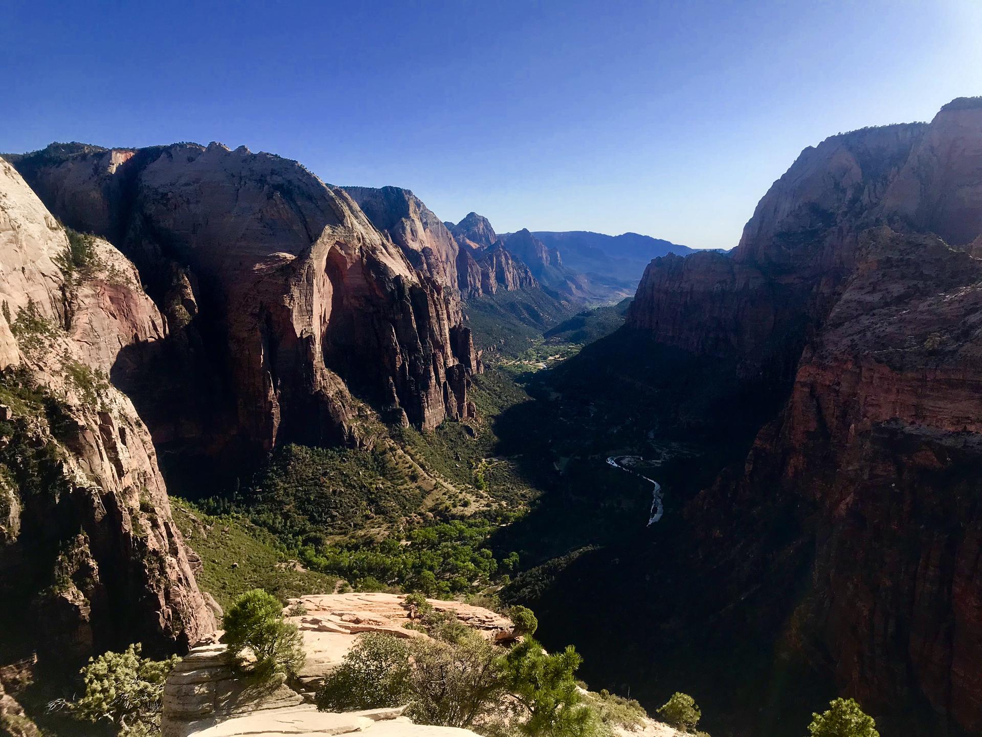 Panoramic view of a deep canyon with winding river and distant mountains at sunset.
