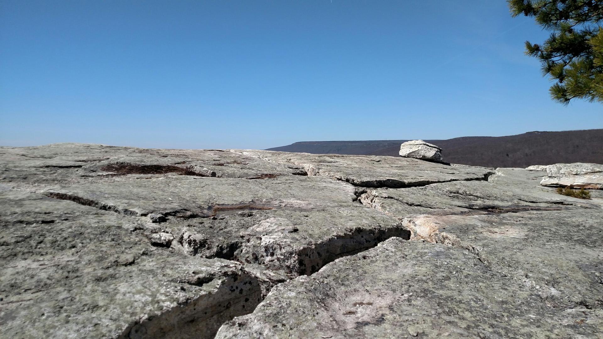 A wide, cracked rock surface with a small rock, overlooking distant mountains.