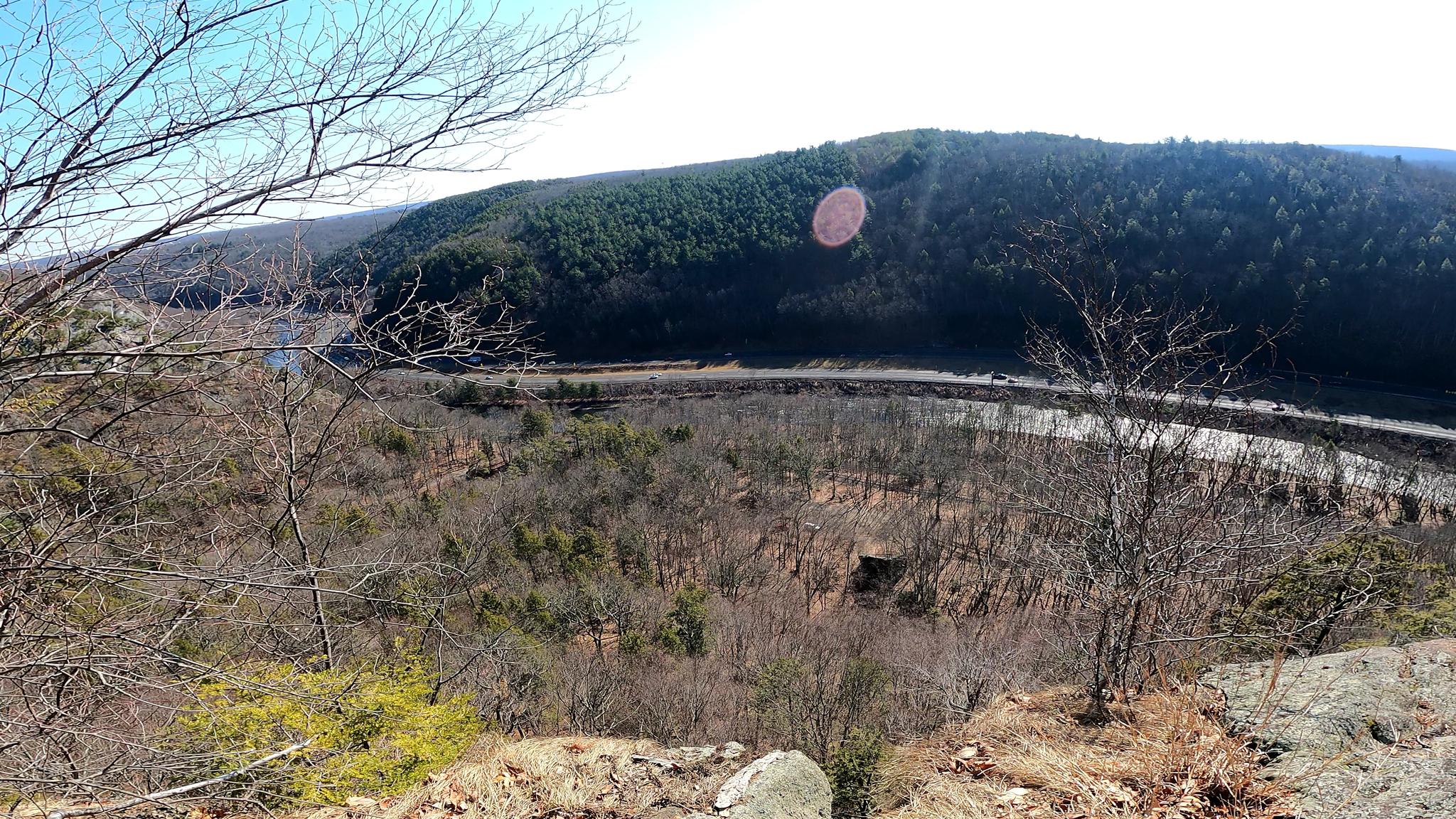 Panoramic view of a winding river through a valley with hills under bright sun.